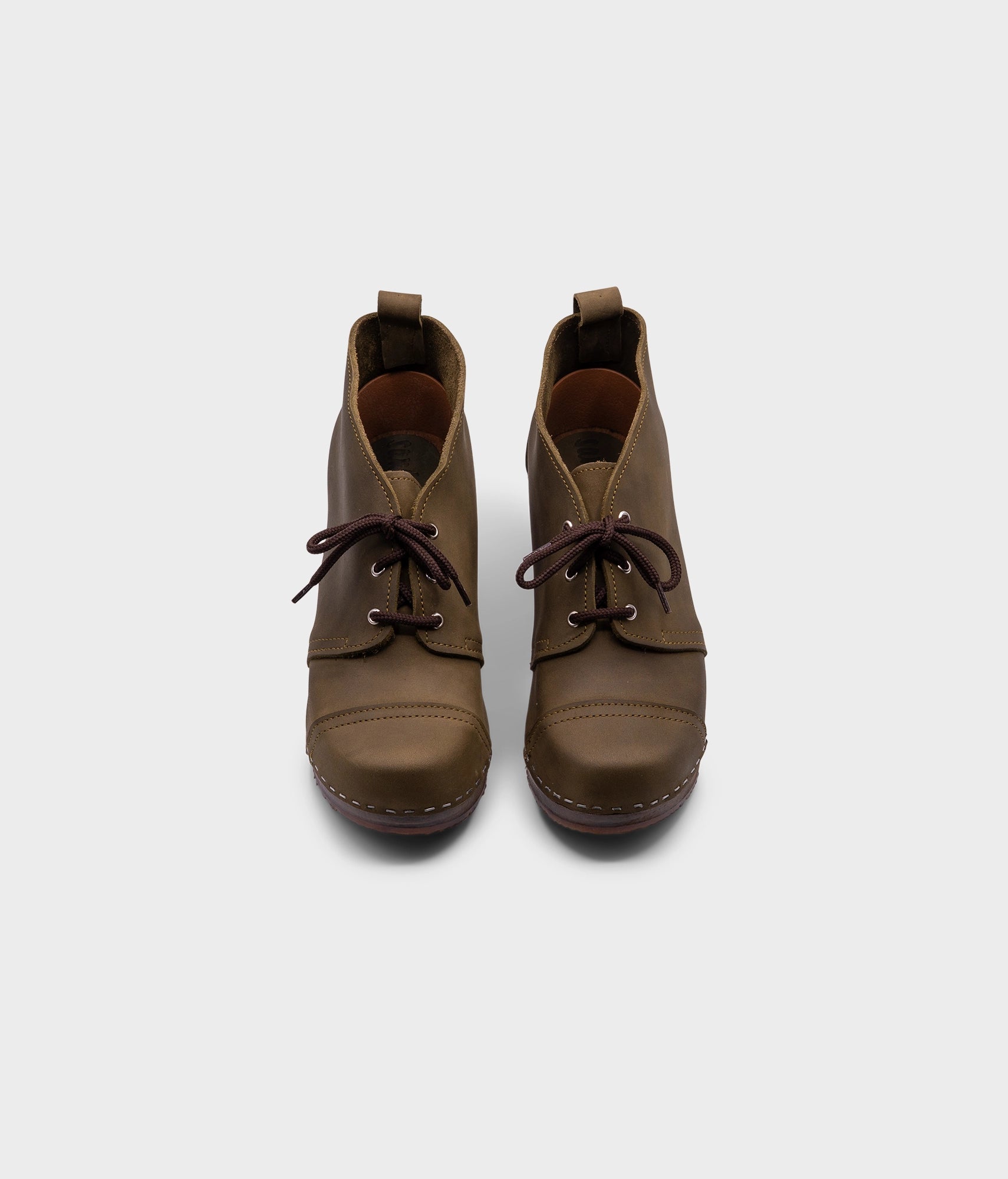 high heeled chukka clog boots in olive green nubuck leather stapled on a dark wooden base with brown laces