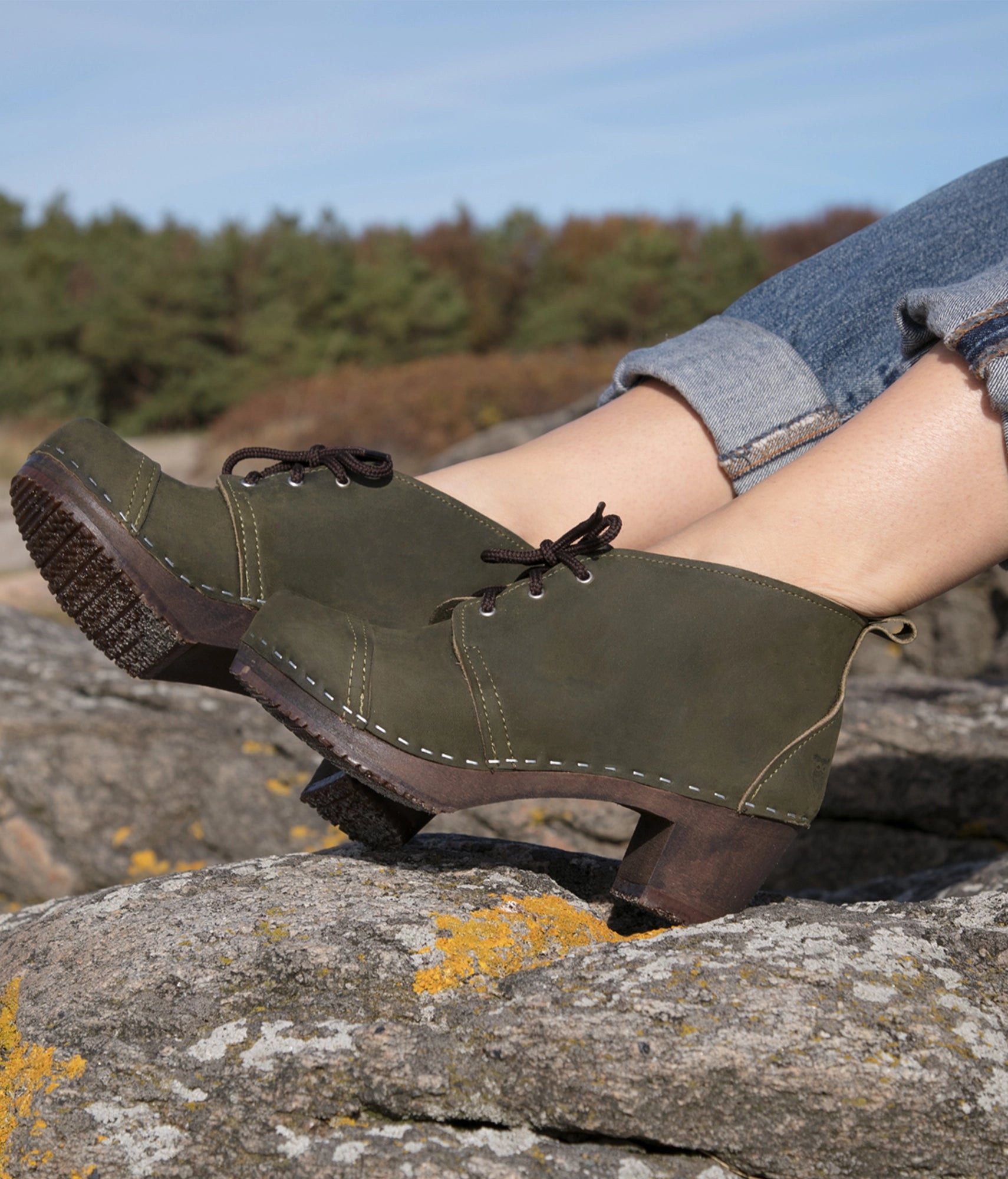 high heeled chukka clog boots in olive green nubuck leather stapled on a dark wooden base with brown laces