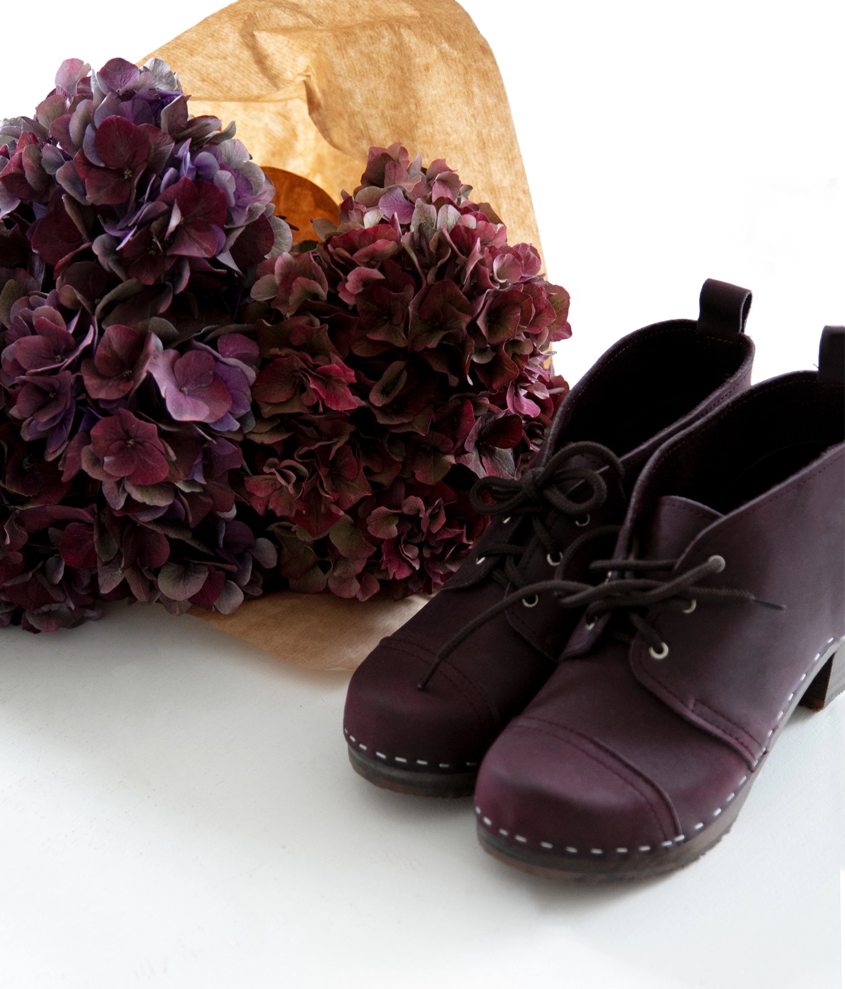 high heeled chukka clog boots in purple plum nubuck leather stapled on a dark wooden base with brown laces