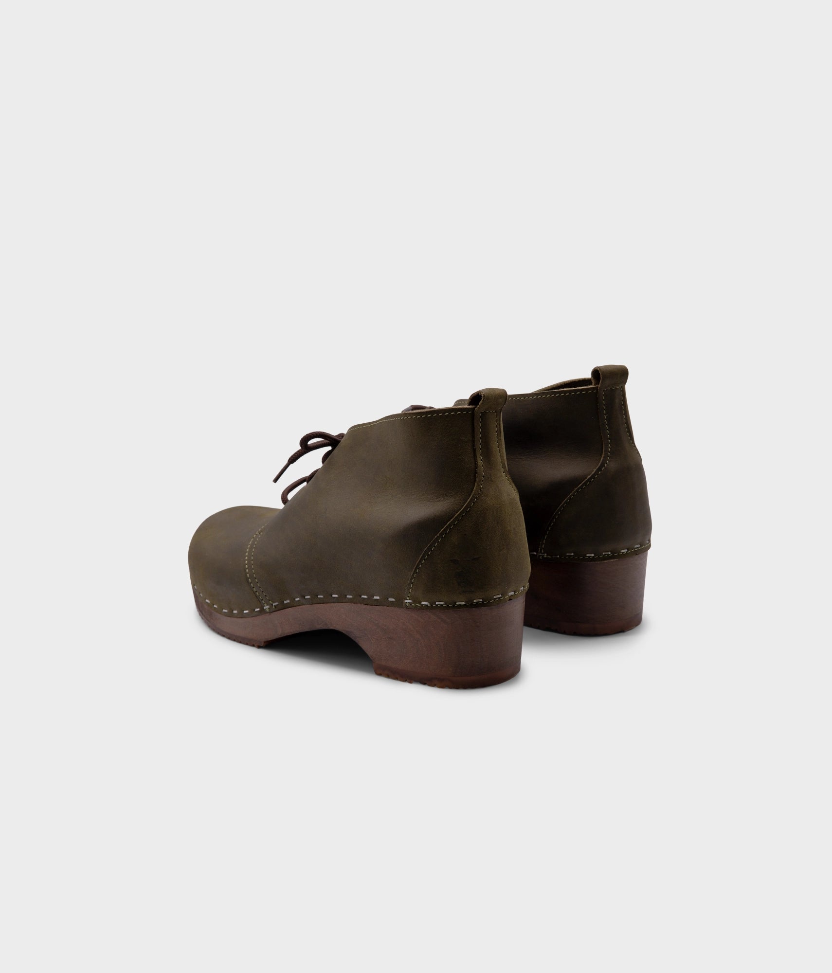 low heeled mens chukka clog boots in olive green nubuck leather stapled on a dark wooden base with brown laces