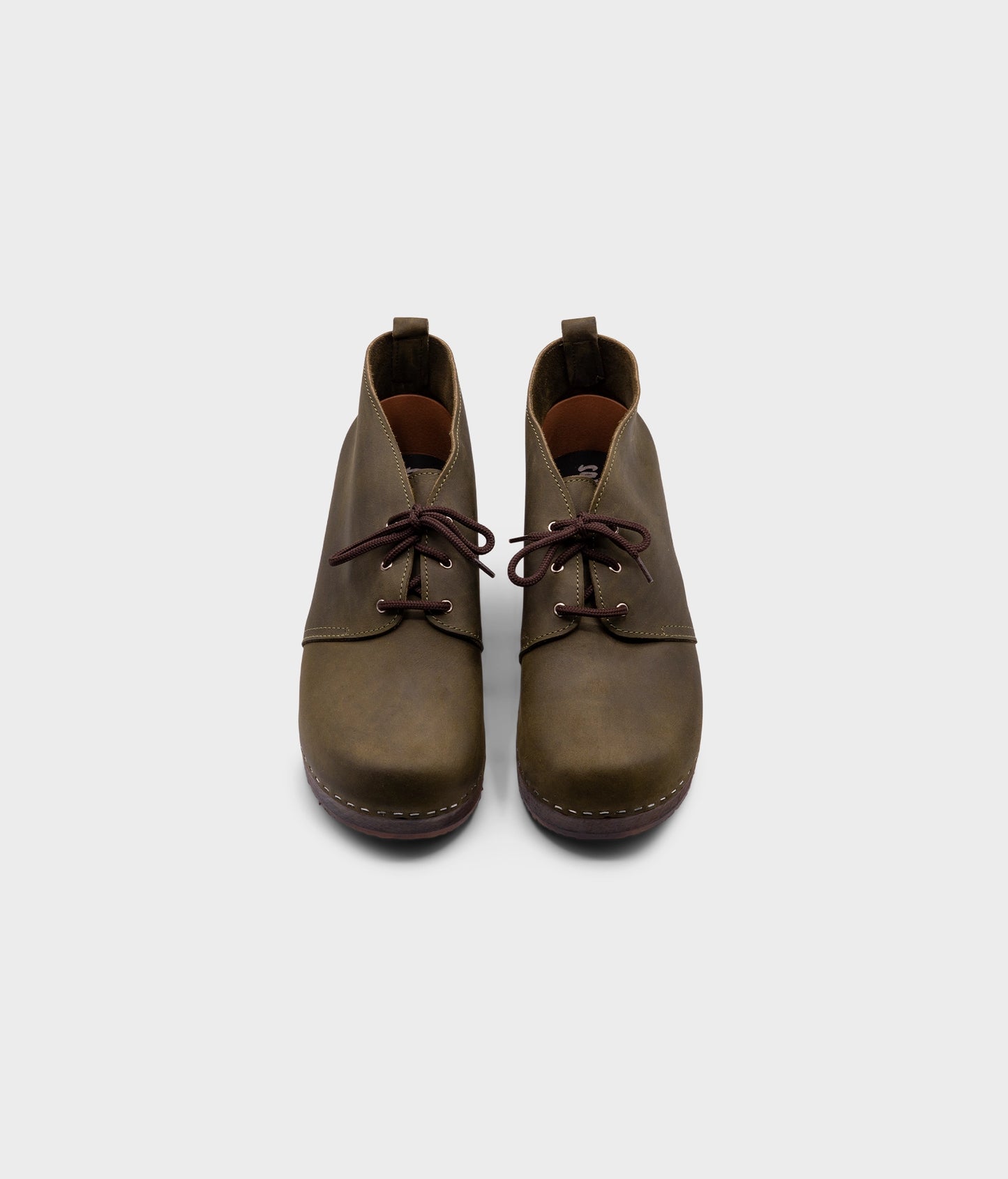 low heeled mens chukka clog boots in olive green nubuck leather stapled on a dark wooden base with brown laces