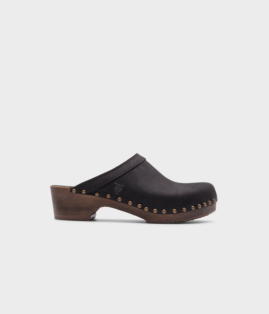 low heeled clog mules in black nubuck leather stapled on a dark wooden base with brass gold studs
