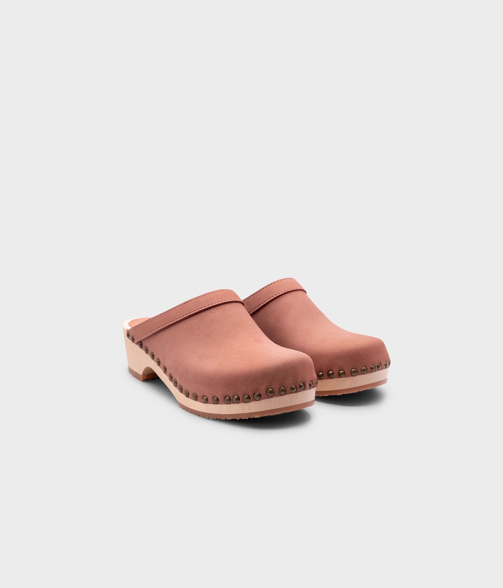 low heeled clog mules in blush pink nubuck leather stapled on a light wooden base with brass gold studs