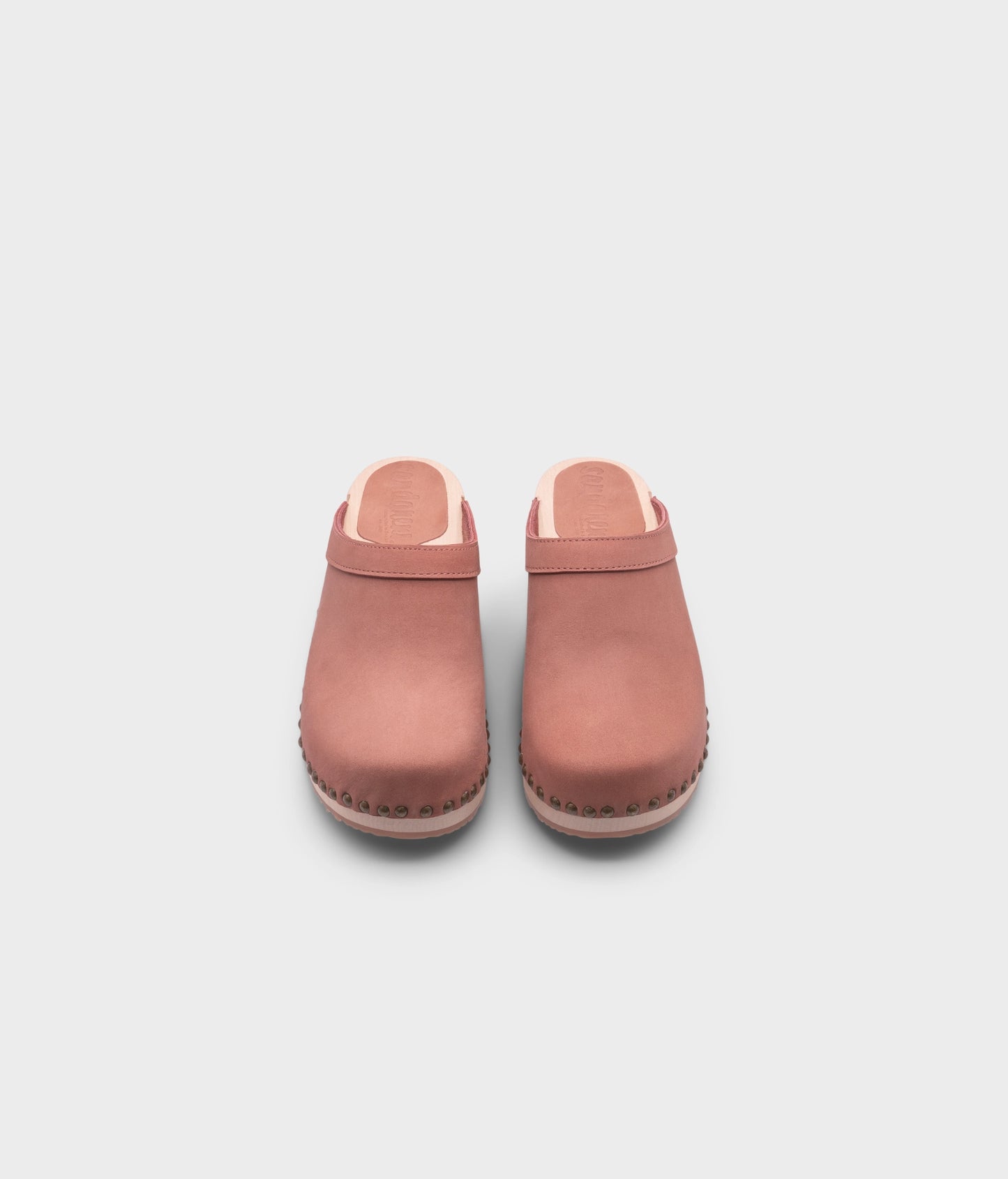 low heeled clog mules in blush pink nubuck leather stapled on a light wooden base with brass gold studs