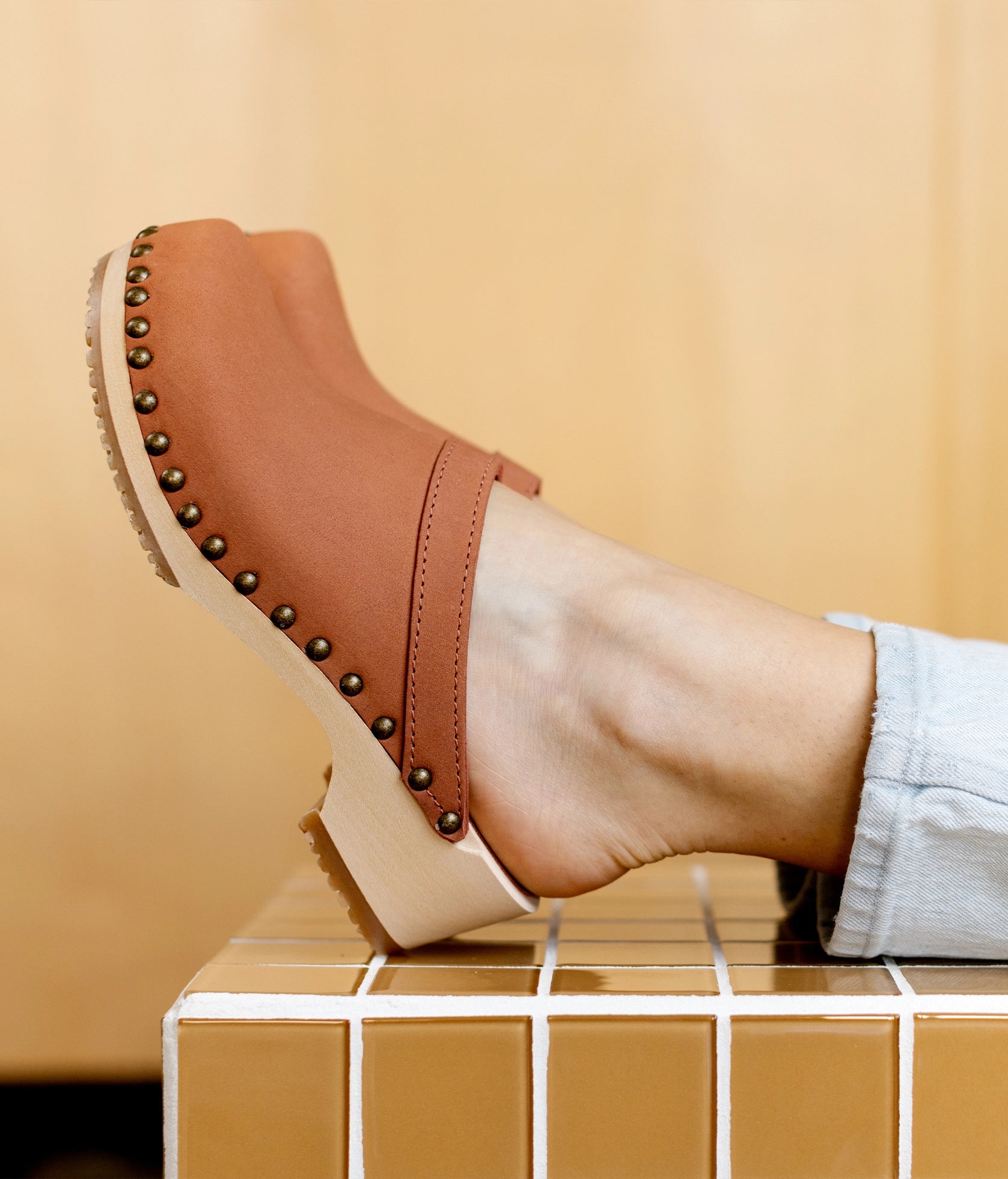low heeled clog mules in blush pink nubuck leather stapled on a light wooden base with brass gold studs
