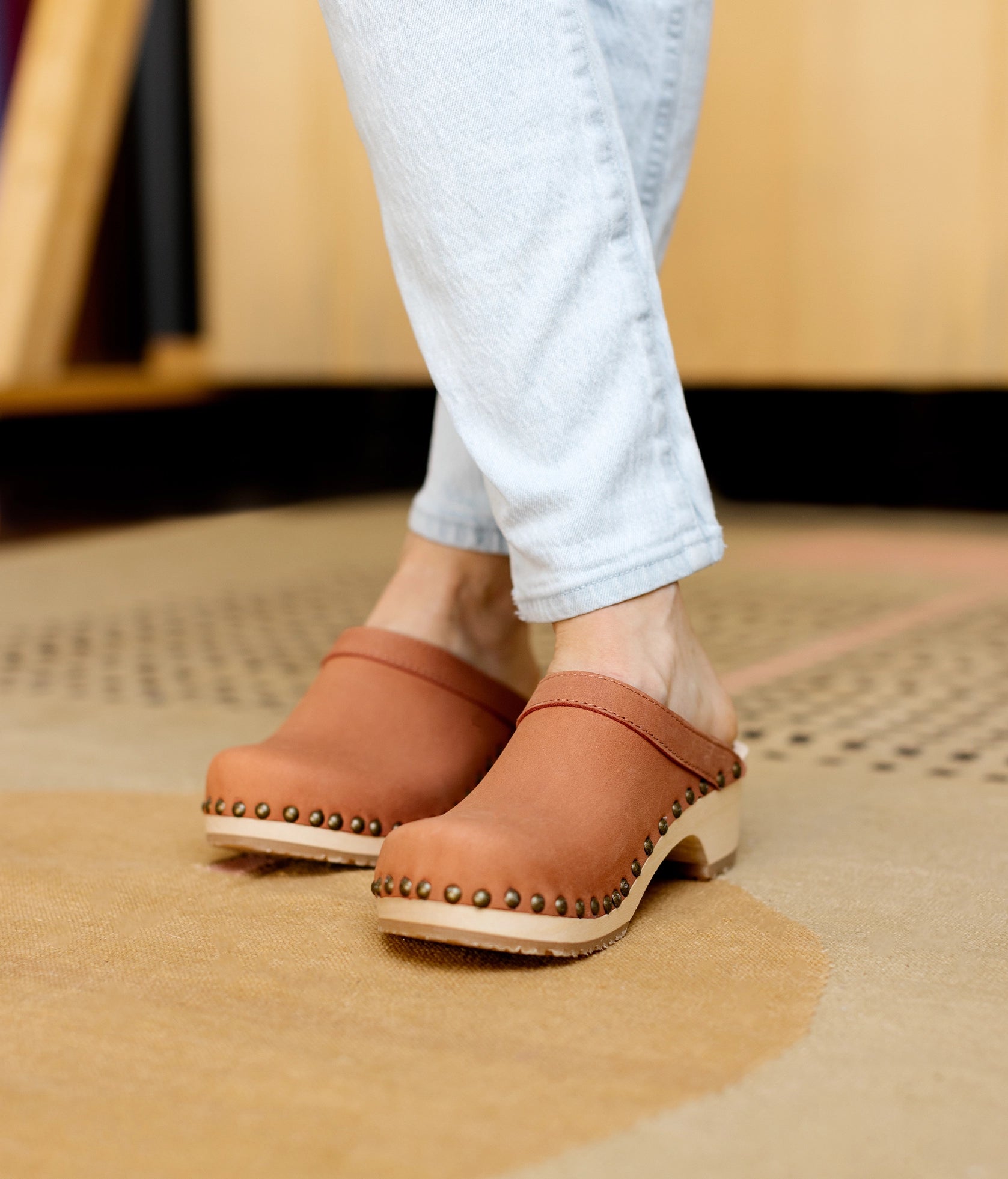 low heeled clog mules in blush pink nubuck leather stapled on a light wooden base with brass gold studs