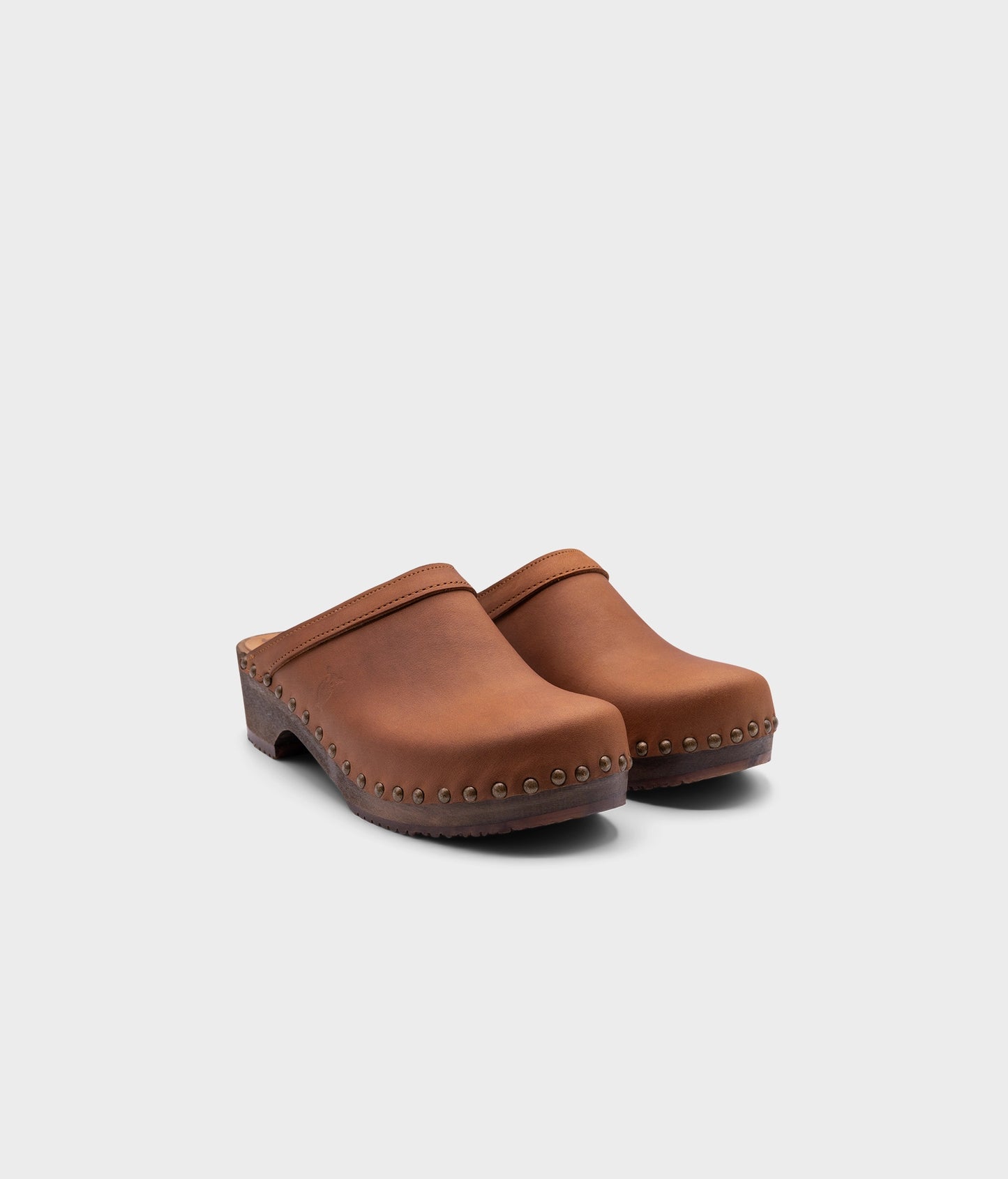 low heeled clog mules in dexter tan nubuck leather stapled on a dark wooden base with brass gold studs