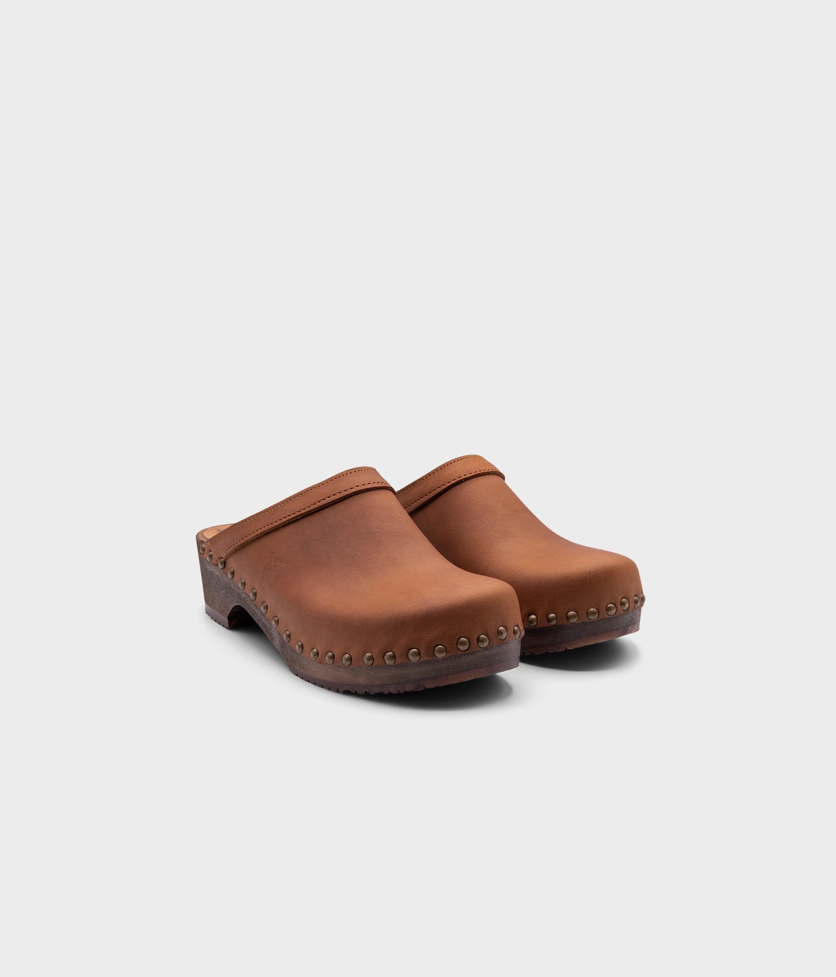 low heeled clog mules in dexter tan nubuck leather stapled on a dark wooden base with brass gold studs
