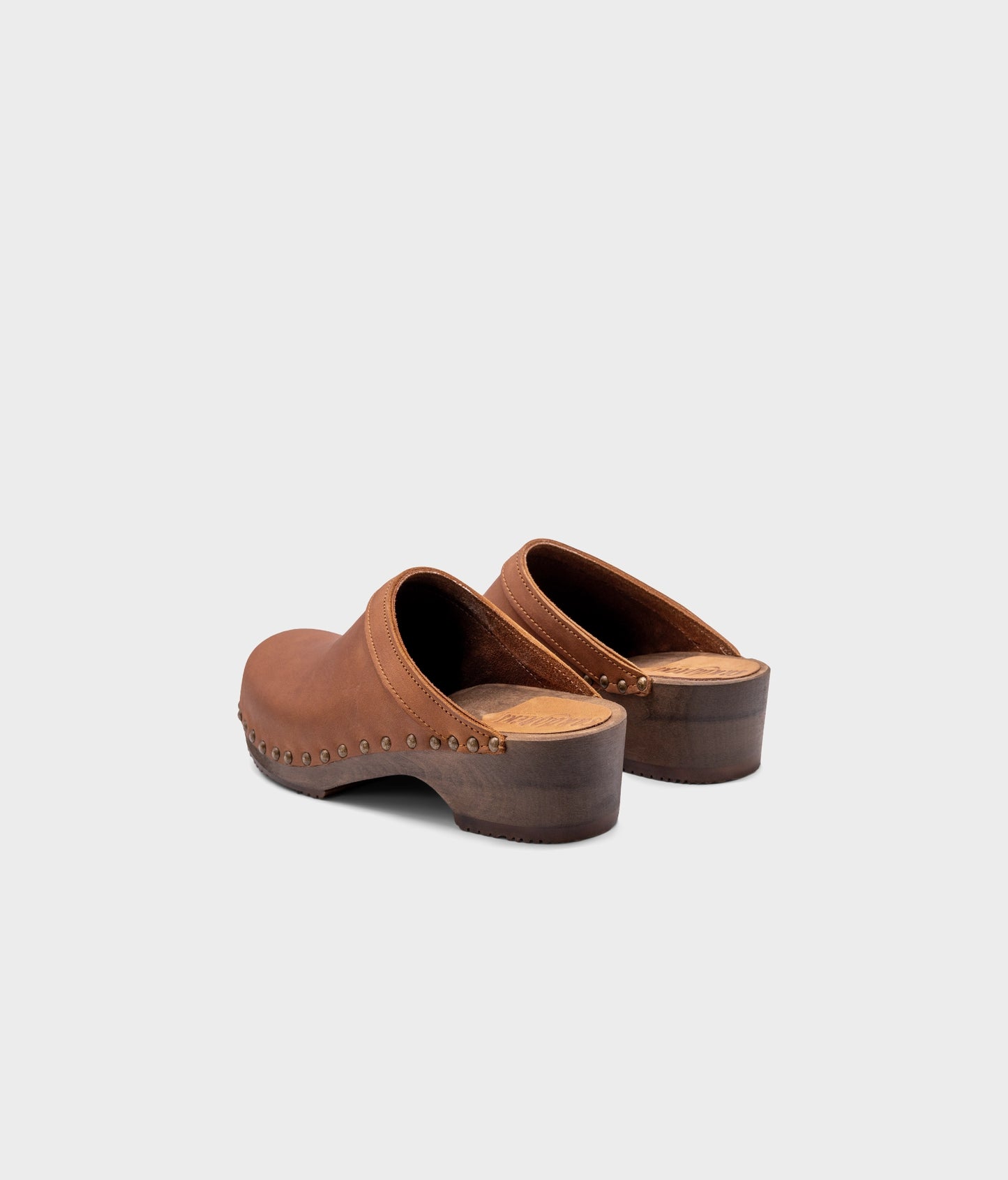 low heeled clog mules in dexter tan nubuck leather stapled on a dark wooden base with brass gold studs