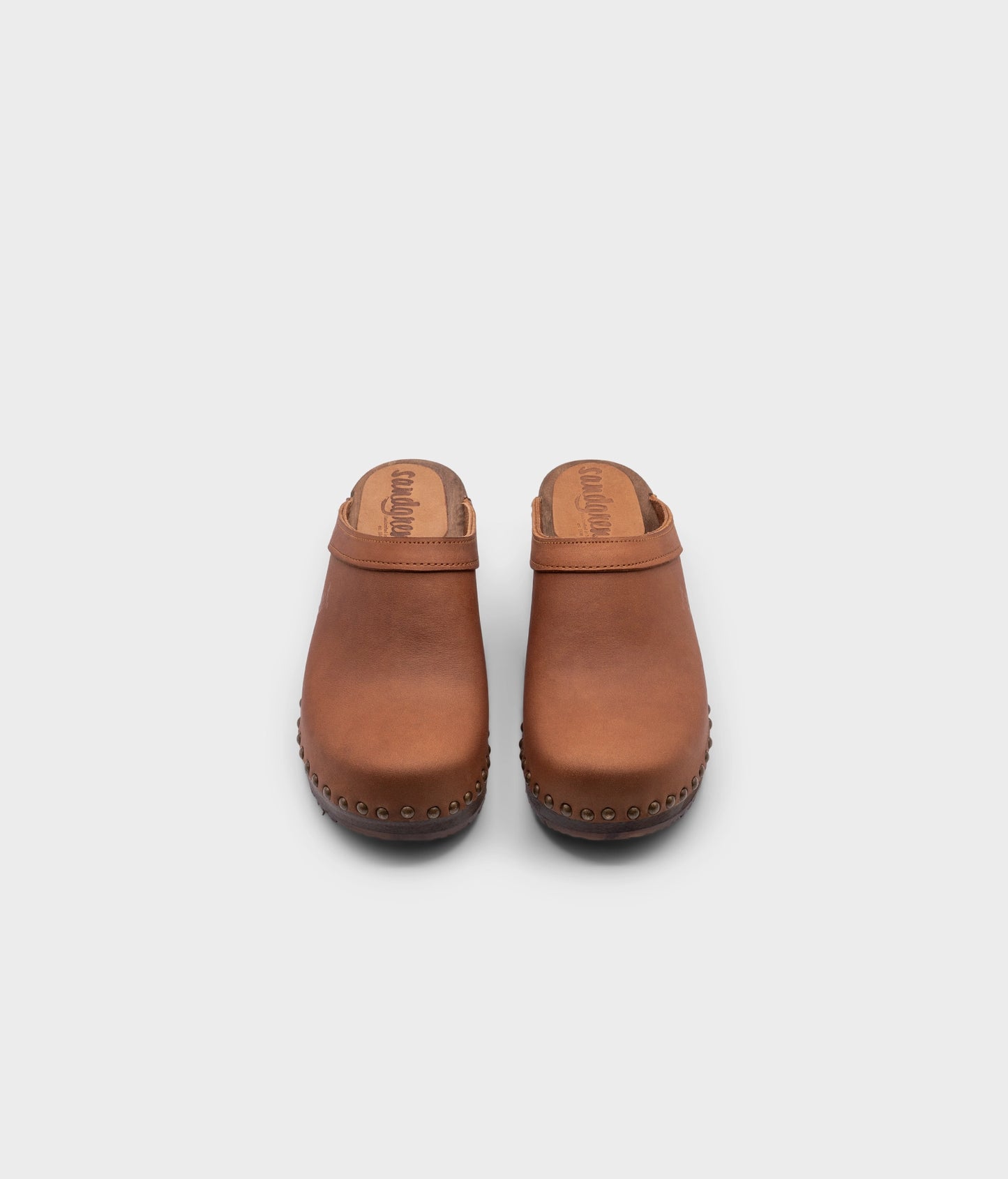 low heeled clog mules in dexter tan nubuck leather stapled on a dark wooden base with brass gold studs