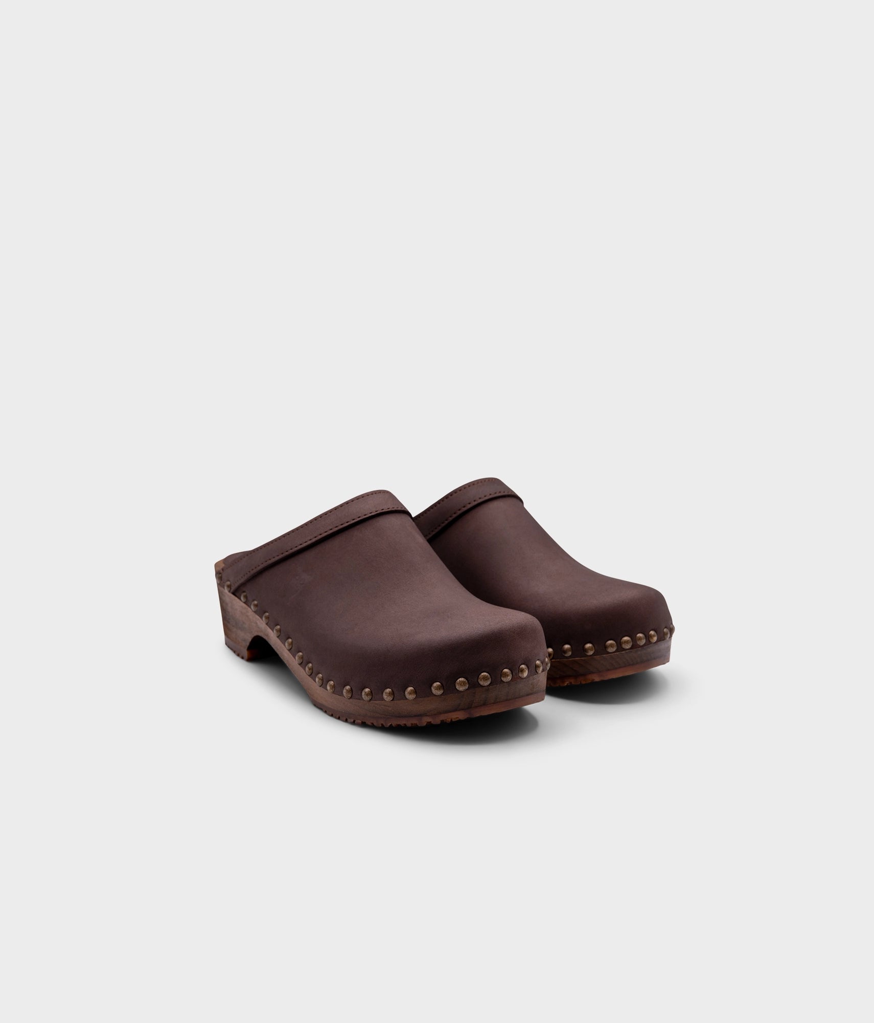 low heeled clog mules in fudge nubuck leather stapled on a dark wooden base with brass gold studs