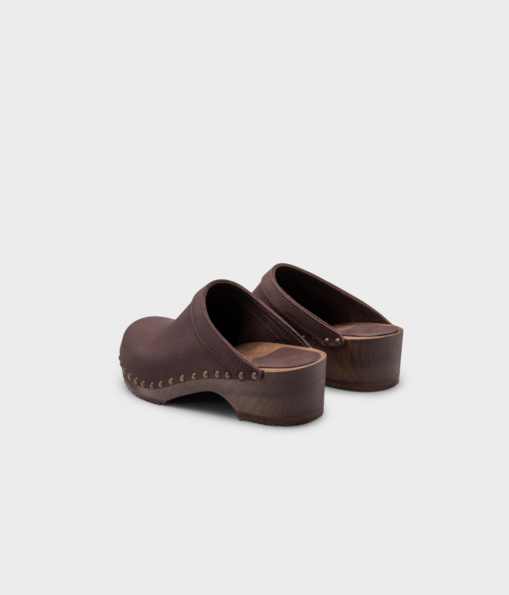 low heeled clog mules in fudge nubuck leather stapled on a dark wooden base with brass gold studs