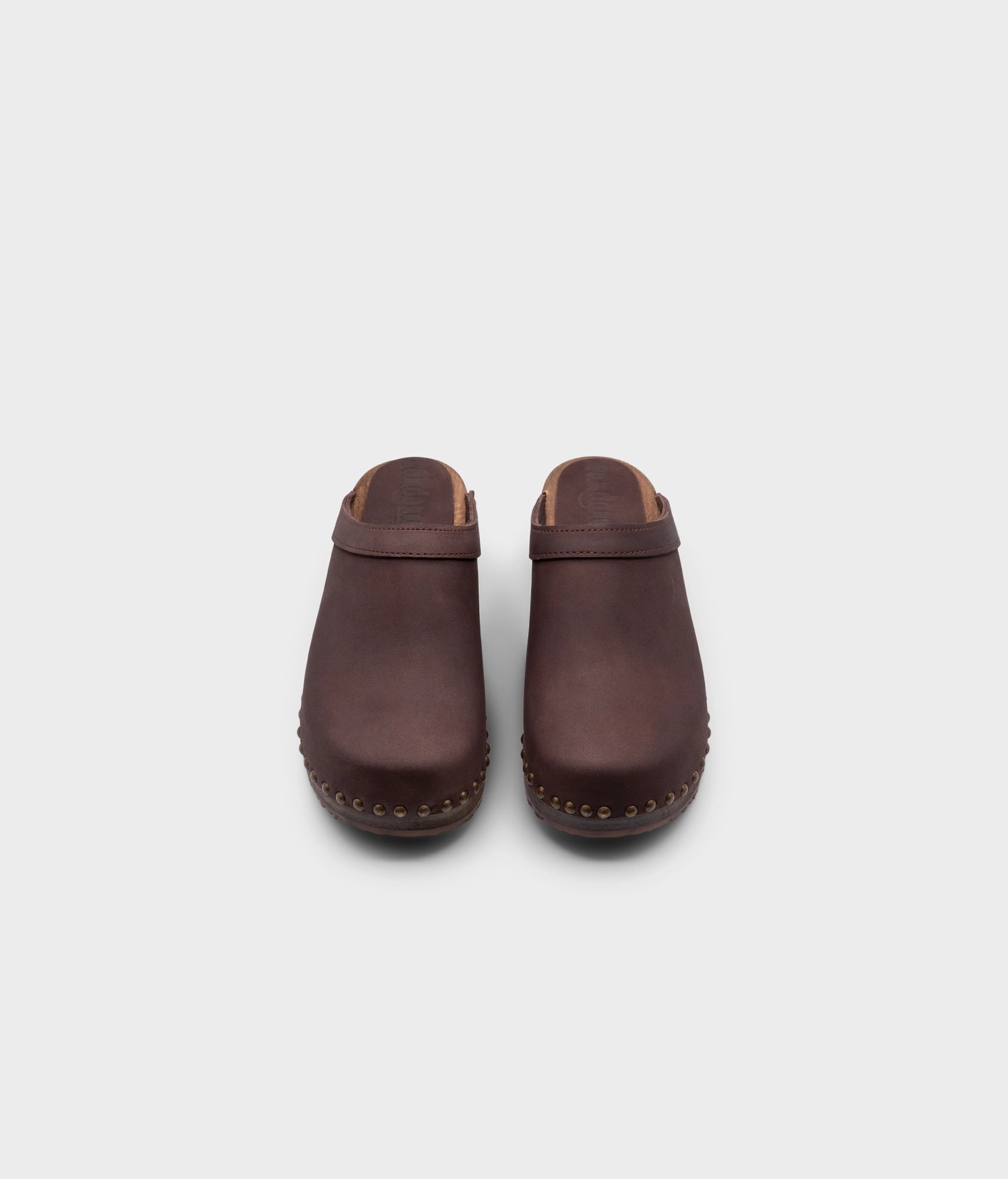 low heeled clog mules in fudge nubuck leather stapled on a dark wooden base with brass gold studs