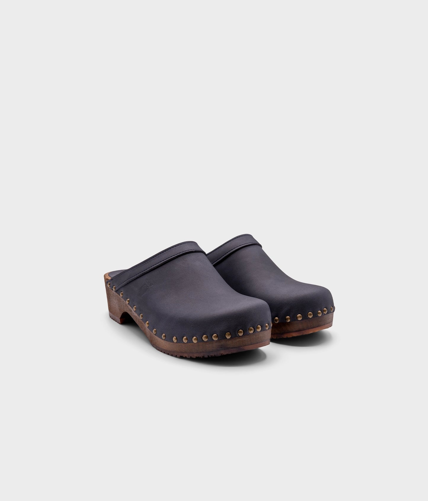 low heeled clog mules in navy nubuck leather stapled on a dark wooden base with brass gold studs