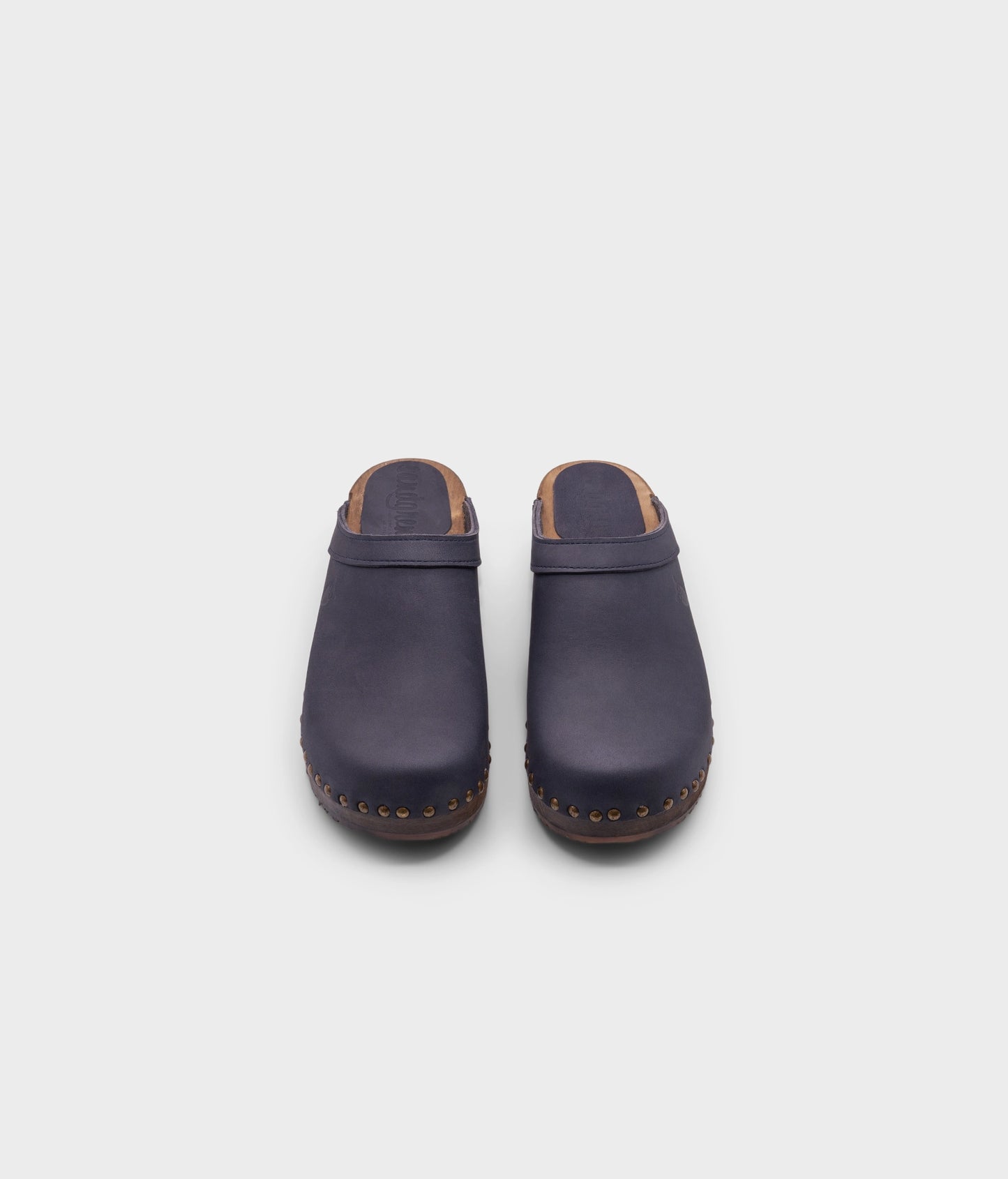 low heeled clog mules in navy nubuck leather stapled on a dark wooden base with brass gold studs