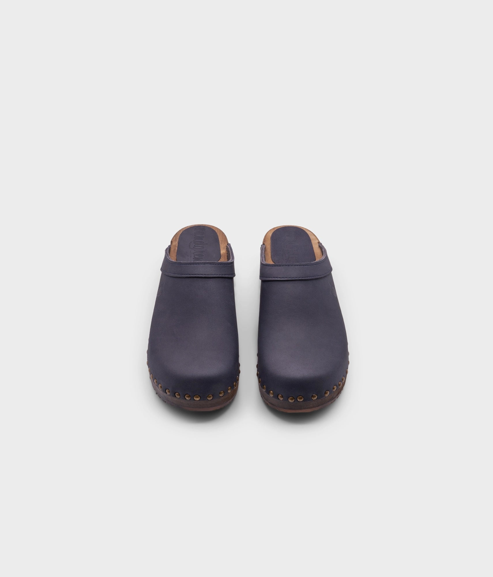 low heeled clog mules in navy nubuck leather stapled on a dark wooden base with brass gold studs