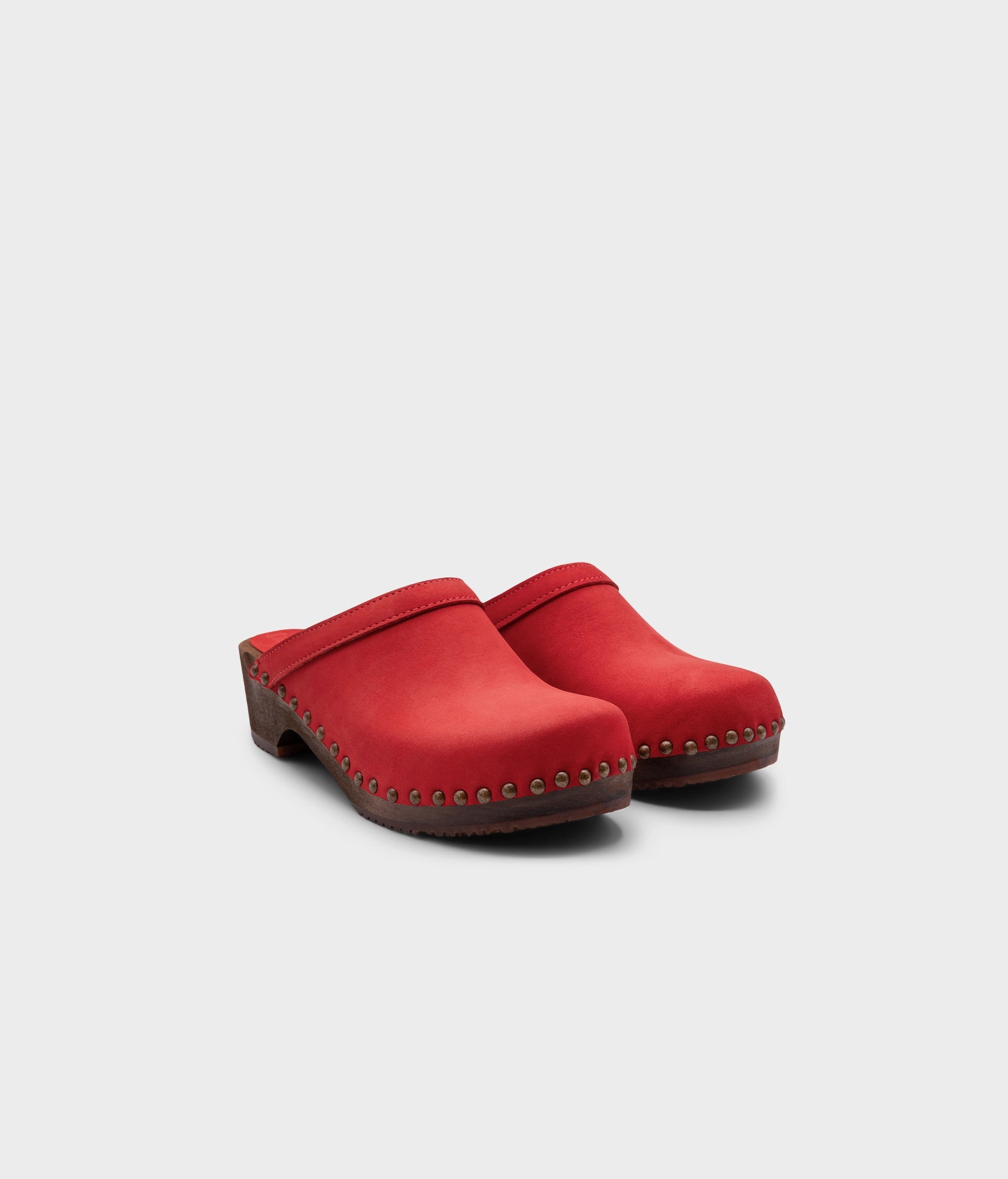 low heeled clog mules in red nubuck leather stapled on a dark wooden base with brass gold studs