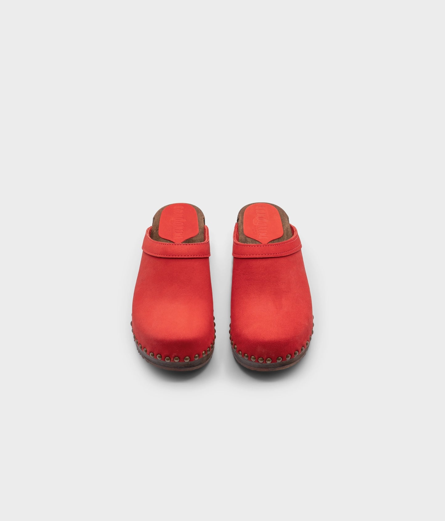 low heeled clog mules in red nubuck leather stapled on a dark wooden base with brass gold studs