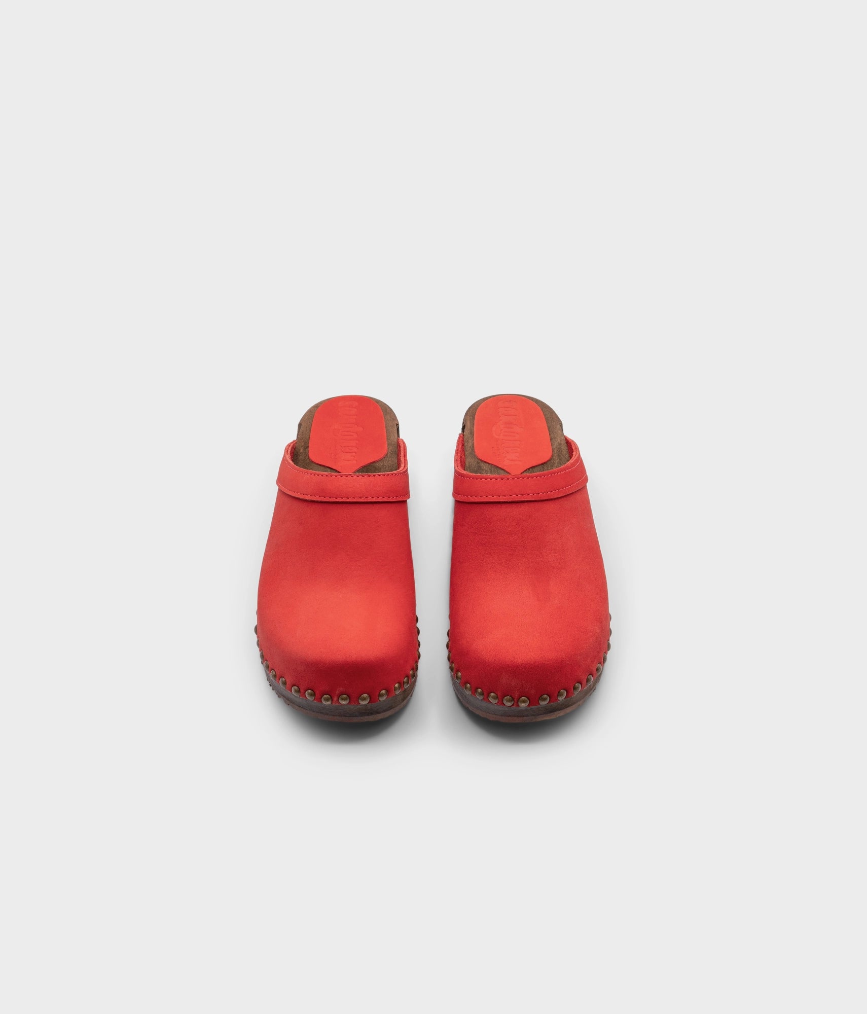 low heeled clog mules in red nubuck leather stapled on a dark wooden base with brass gold studs
