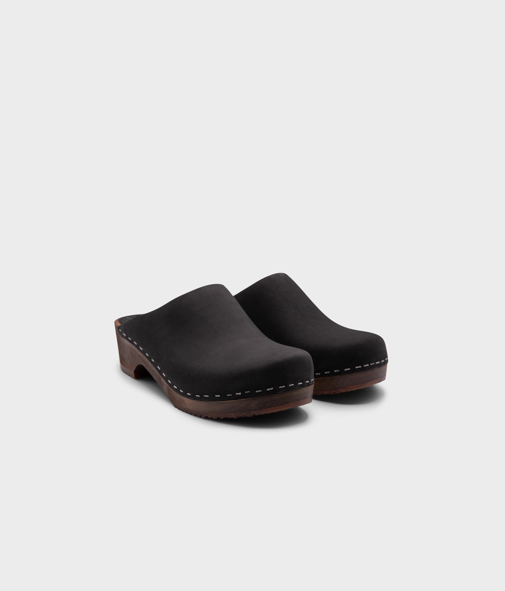 low heeled minimalistic clog mules in black nubuck leather stapled on a dark wooden base