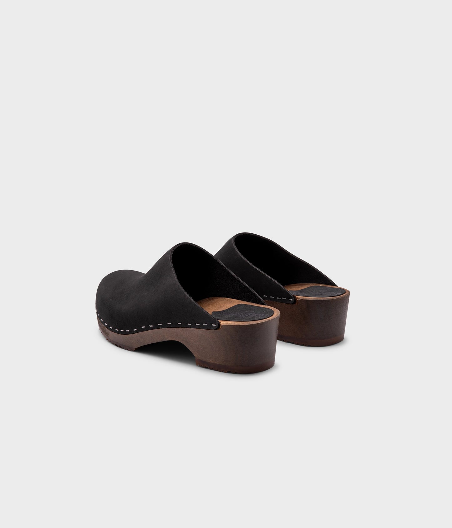 low heeled minimalistic clog mules in black nubuck leather stapled on a dark wooden base