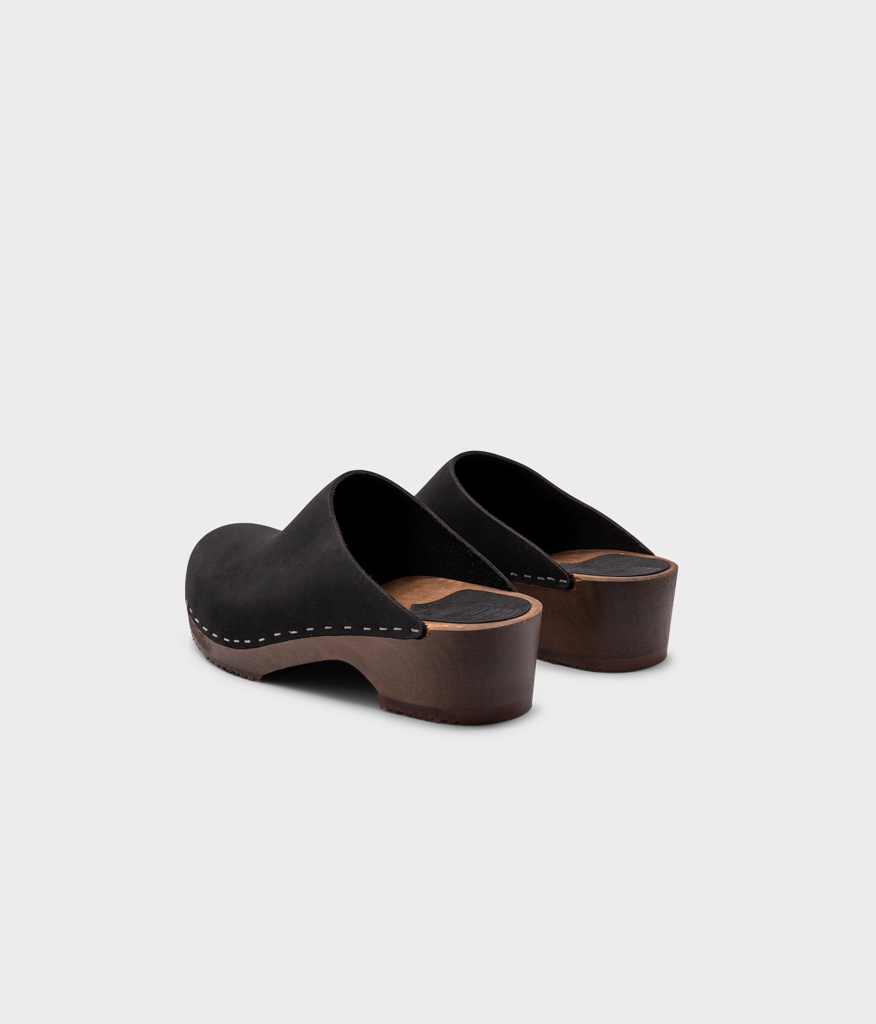 low heeled minimalistic clog mules in black nubuck leather stapled on a dark wooden base