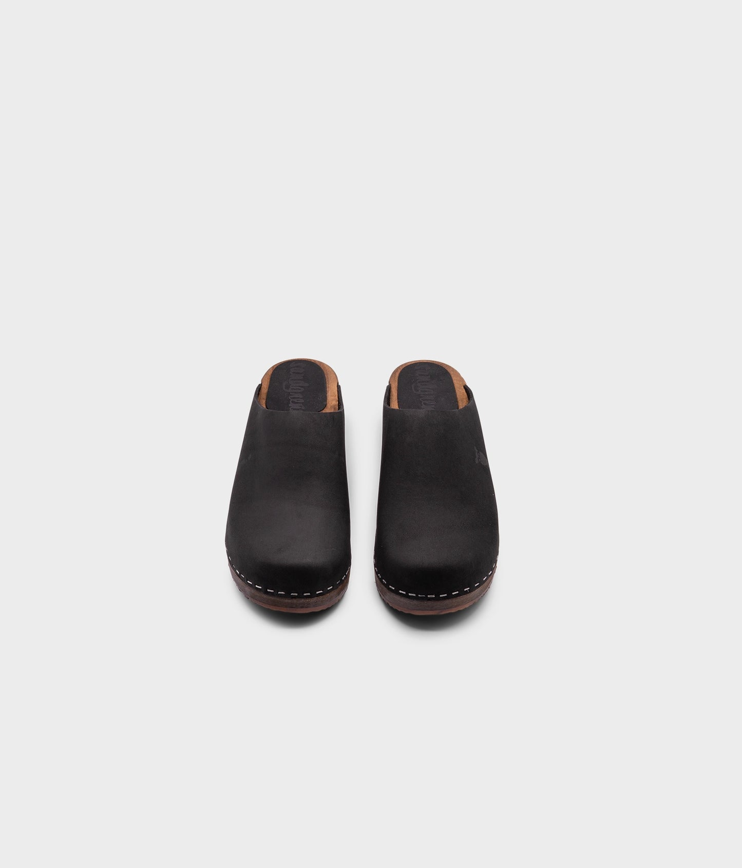 low heeled minimalistic clog mules in black nubuck leather stapled on a dark wooden base