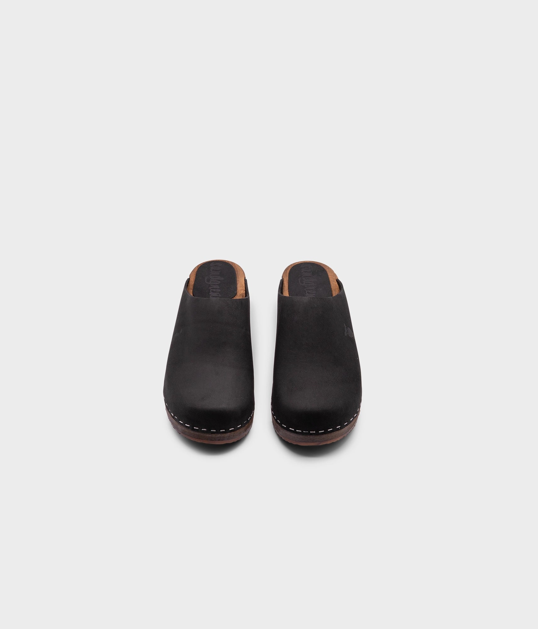 low heeled minimalistic clog mules in black nubuck leather stapled on a dark wooden base