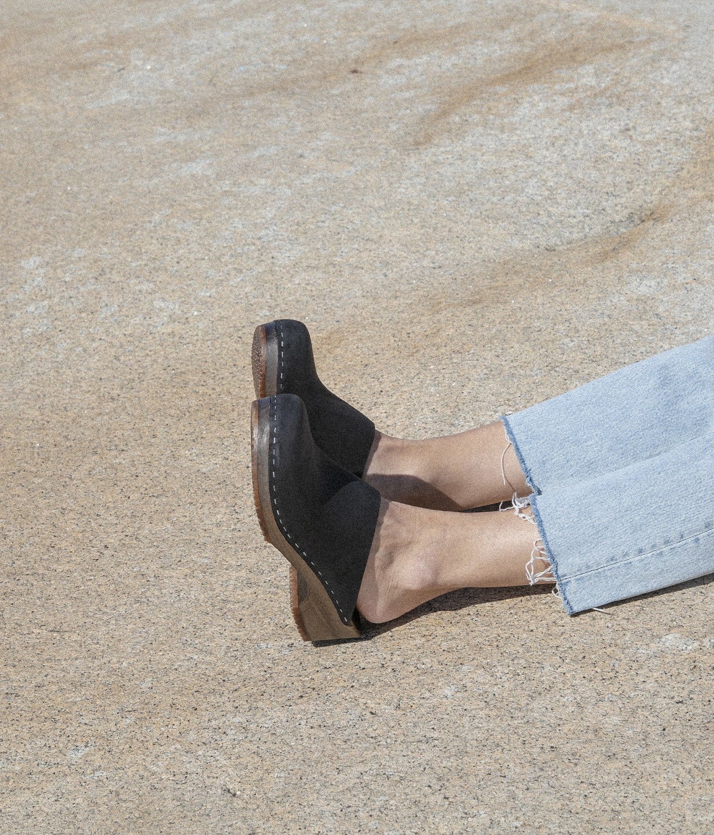 low heeled minimalistic clog mules in black nubuck leather stapled on a dark wooden base