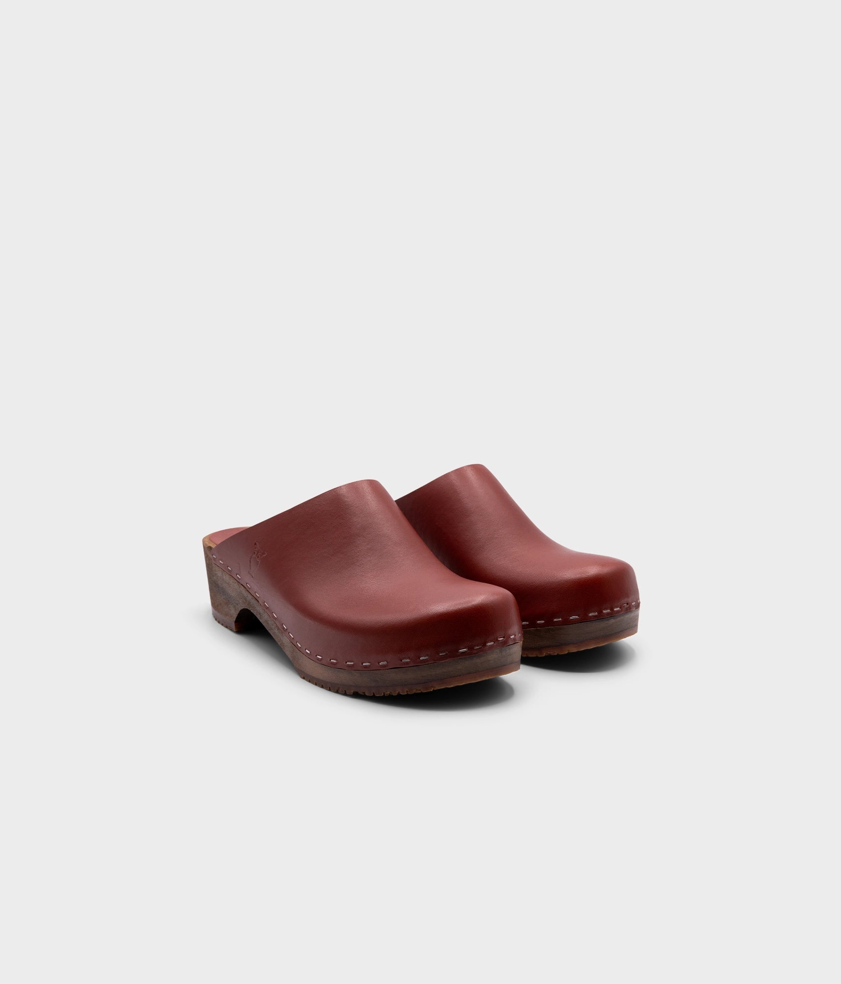 low heeled minimalistic clog mules in cognac vegetable tanned leather stapled on a dark wooden base