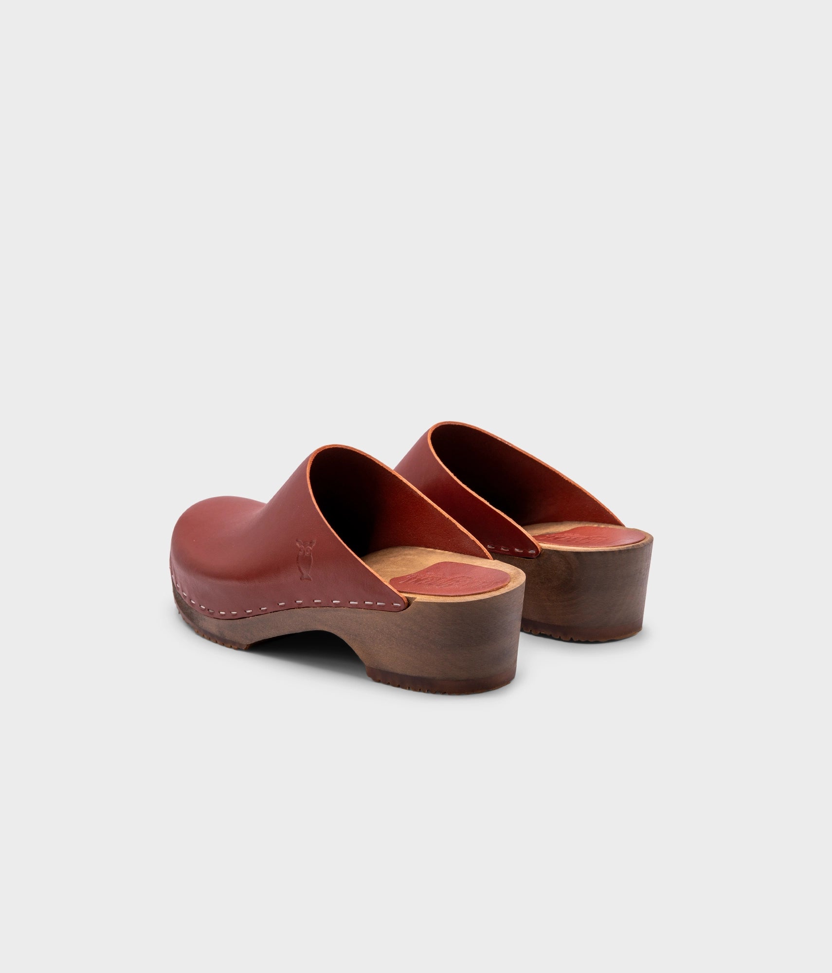 low heeled minimalistic clog mules in cognac vegetable tanned leather stapled on a dark wooden base
