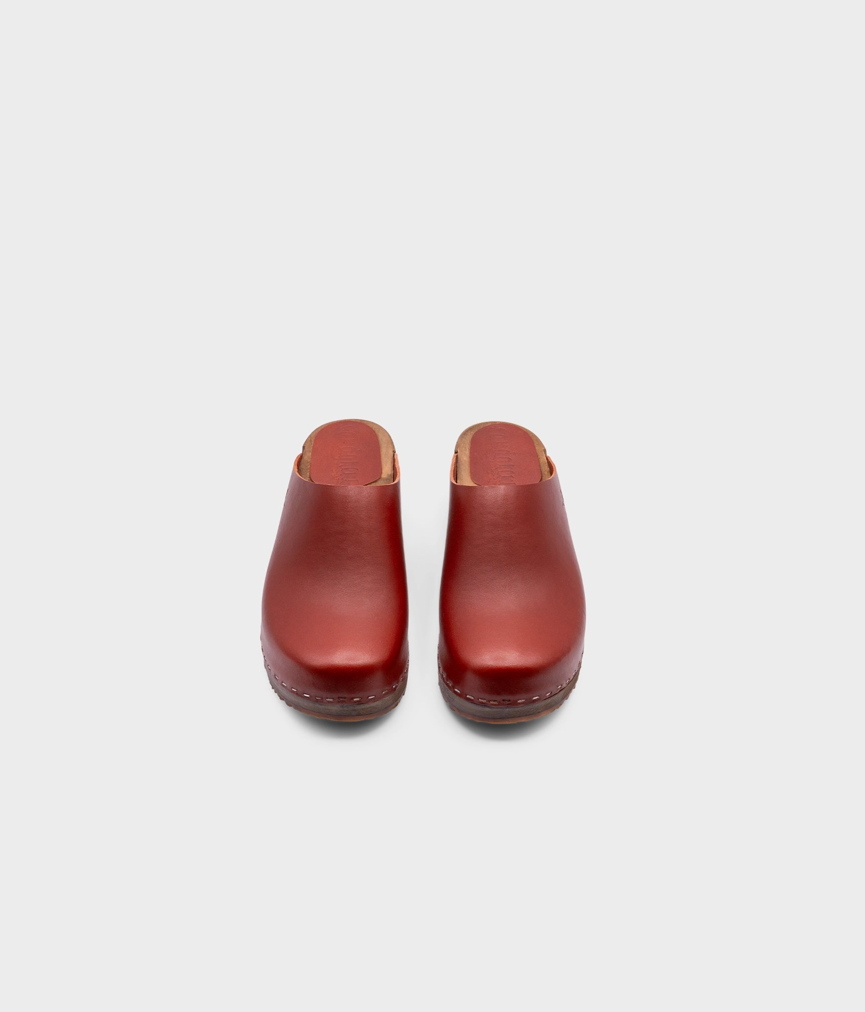 low heeled minimalistic clog mules in cognac vegetable tanned leather stapled on a dark wooden base