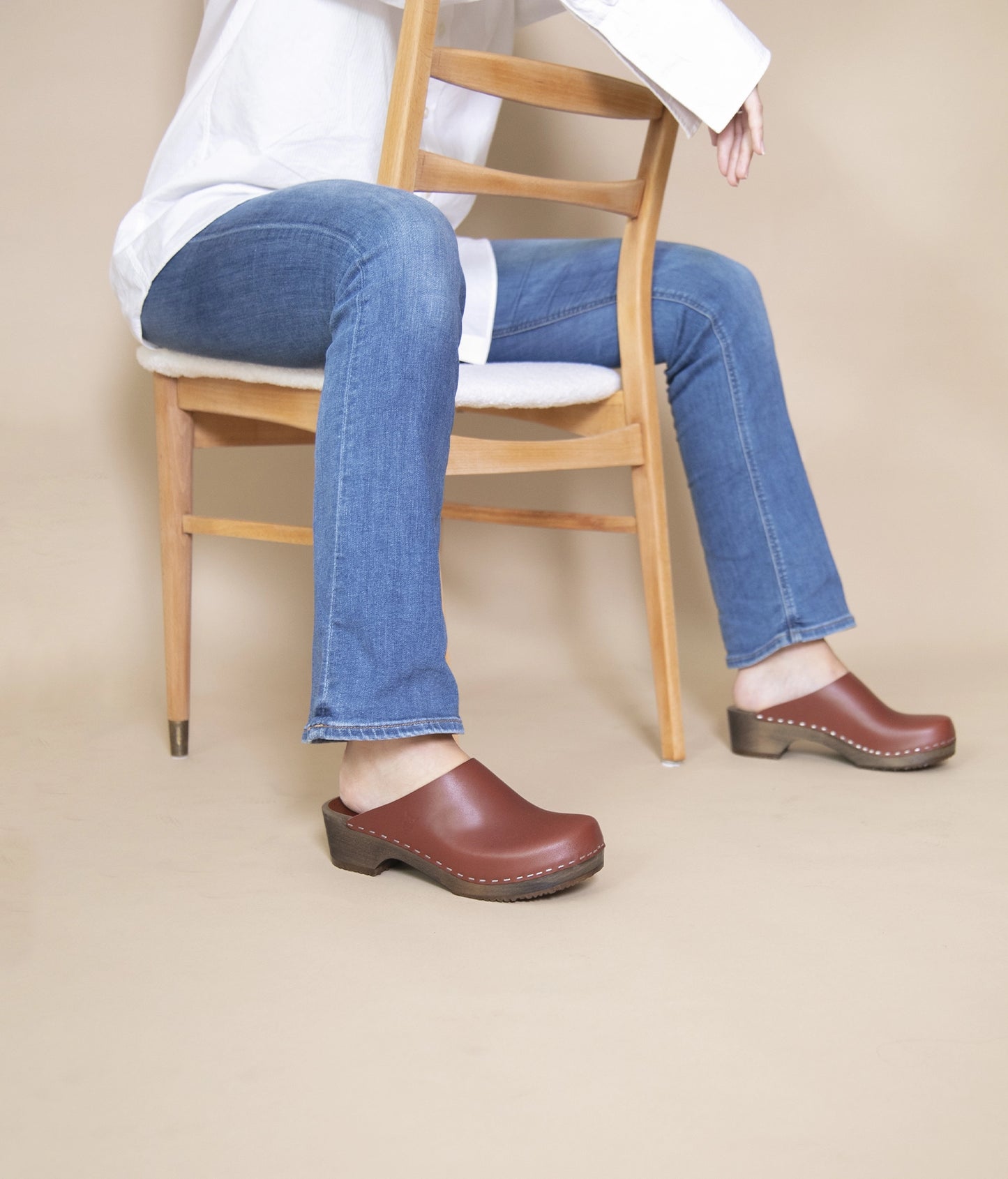 low heeled minimalistic clog mules in cognac vegetable tanned leather stapled on a dark wooden base