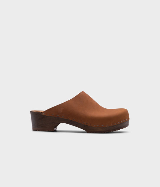 low heeled minimalistic clog mules in dexter tan nubuck leather stapled on a dark wooden base