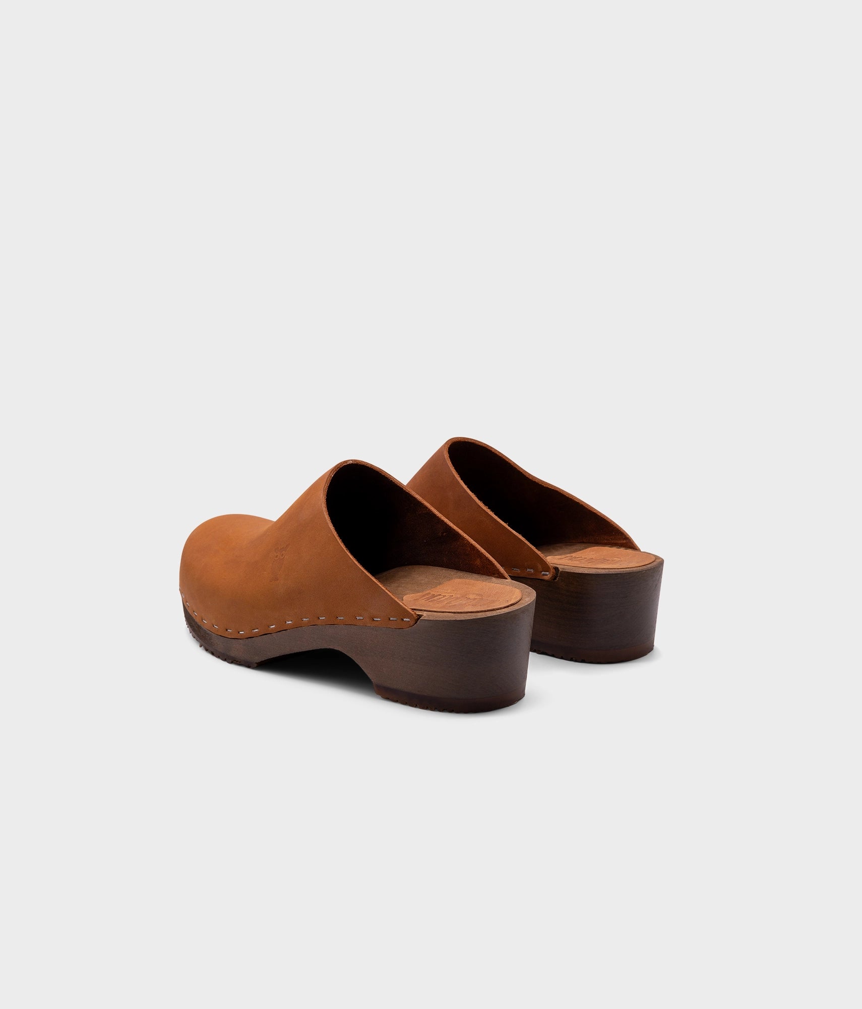 low heeled minimalistic clog mules in dexter tan nubuck leather stapled on a dark wooden base