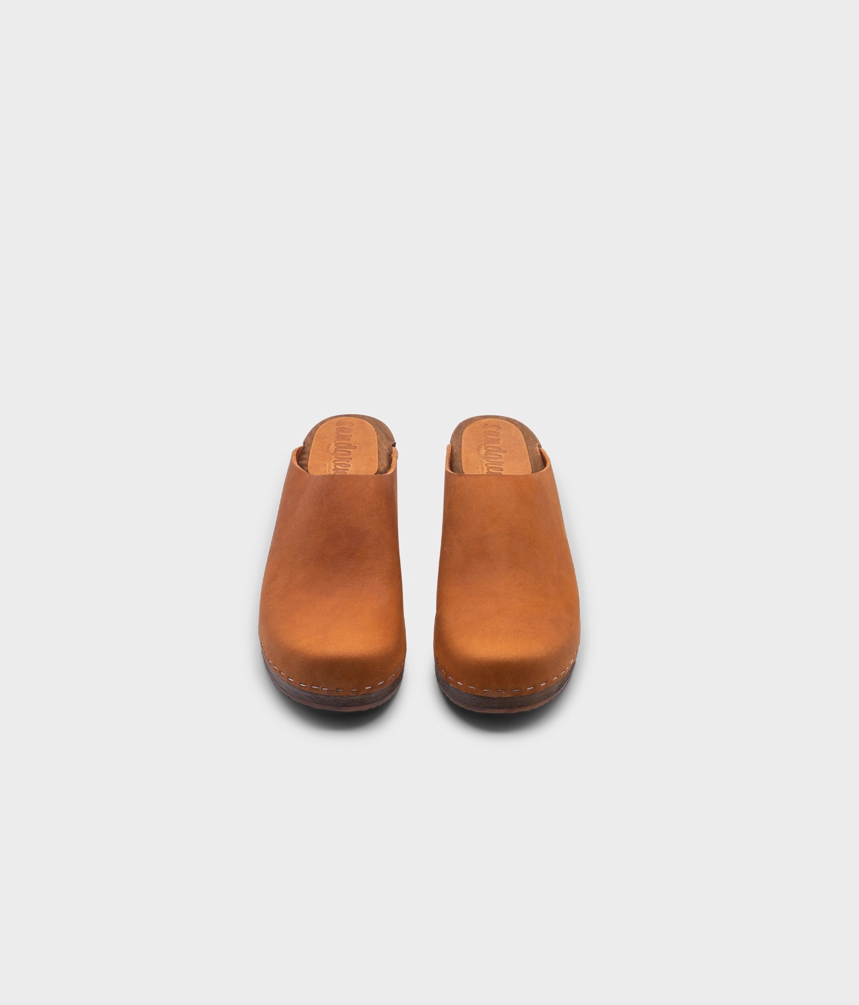 low heeled minimalistic clog mules in dexter tan nubuck leather stapled on a dark wooden base
