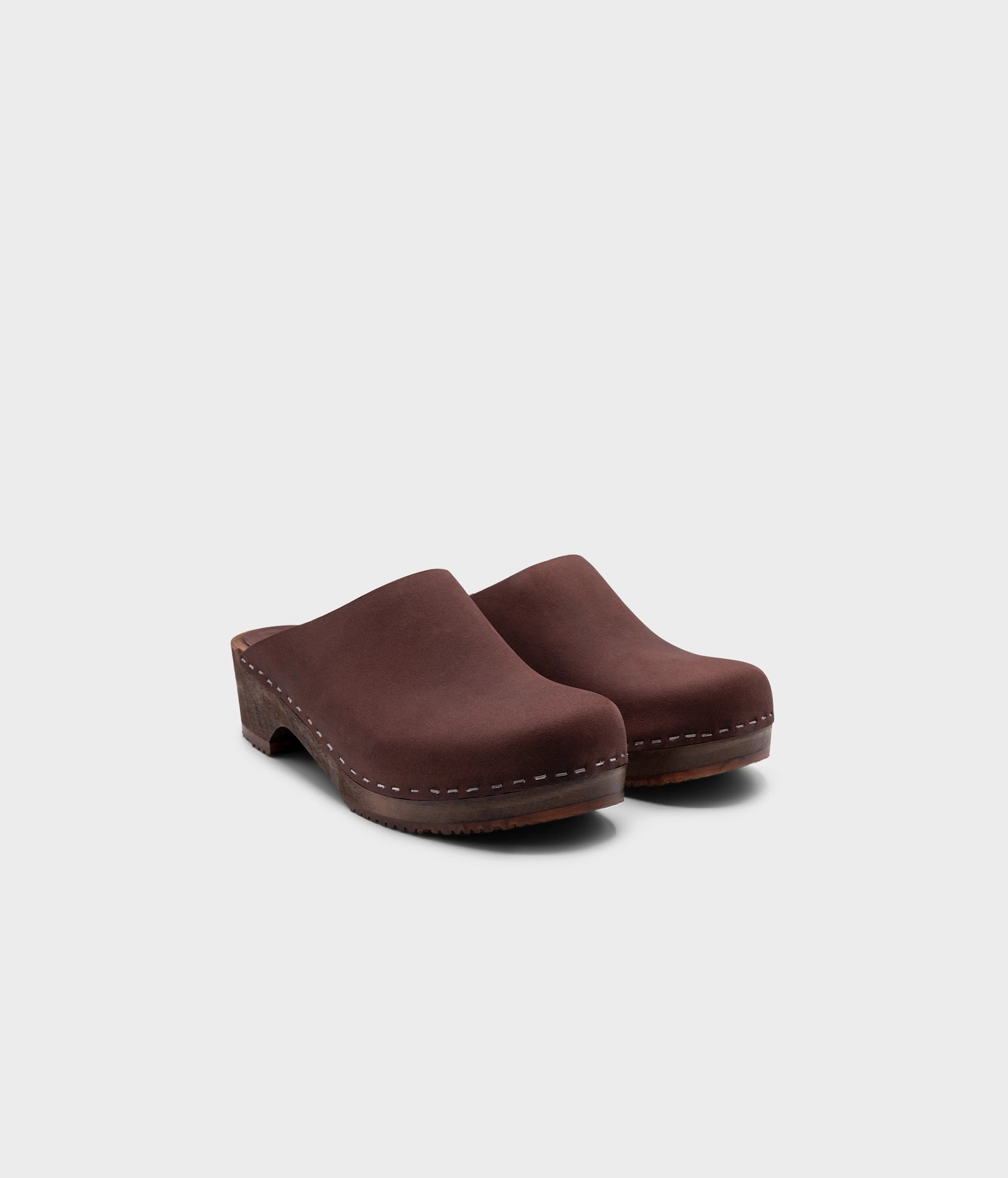 low heeled minimalistic clog mules in fudge nubuck leather stapled on a dark wooden base