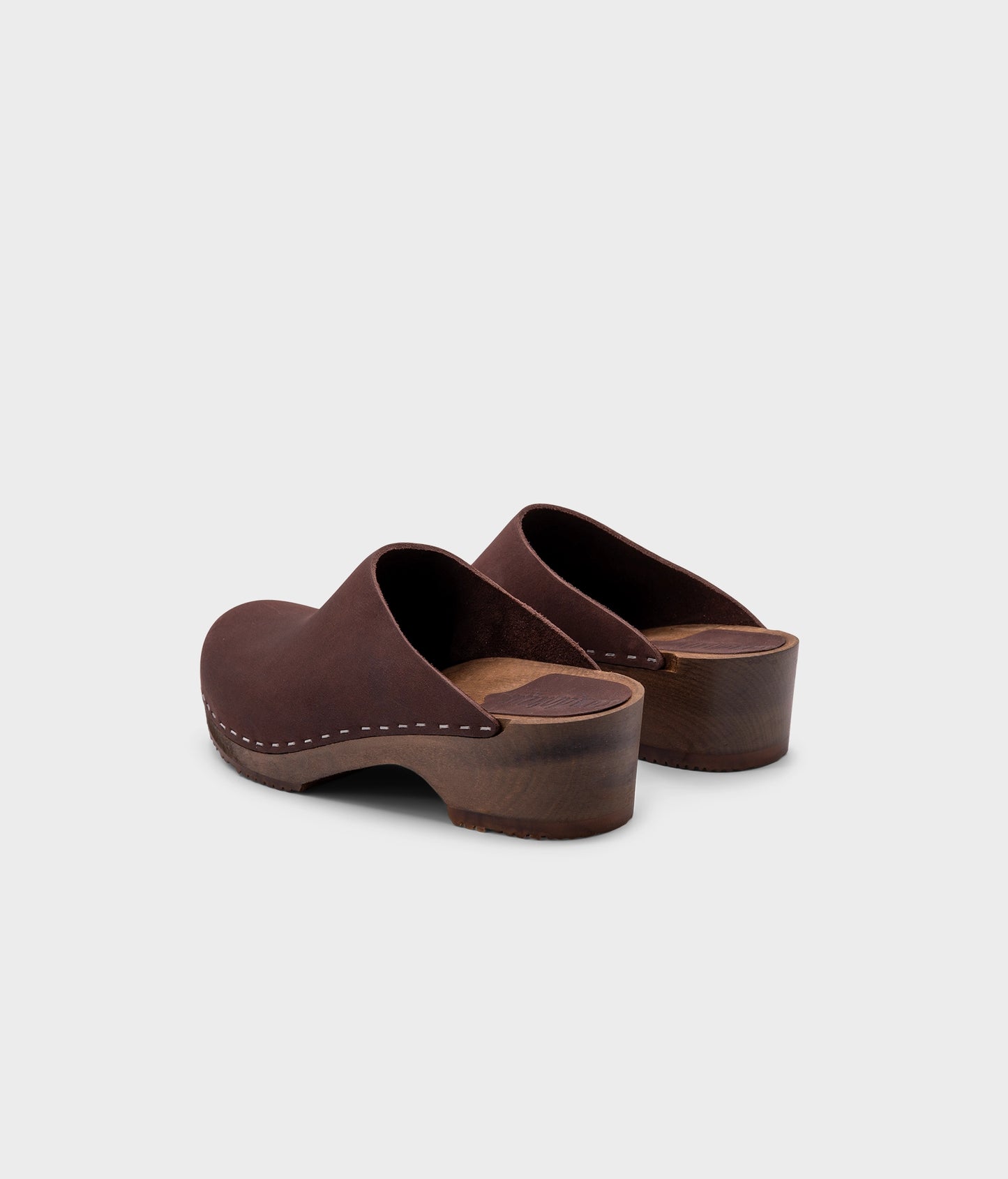 low heeled minimalistic clog mules in fudge nubuck leather stapled on a dark wooden base