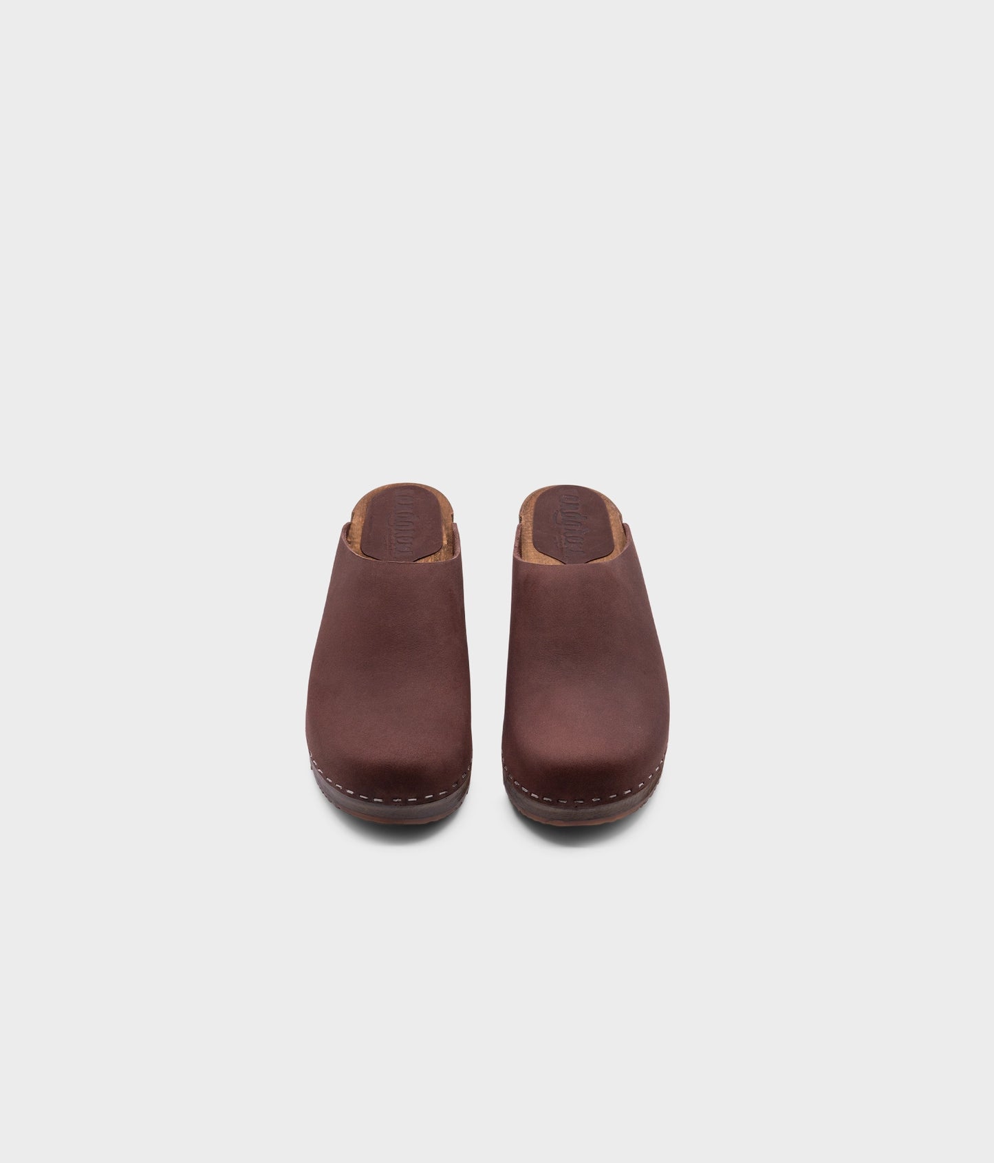 low heeled minimalistic clog mules in fudge nubuck leather stapled on a dark wooden base