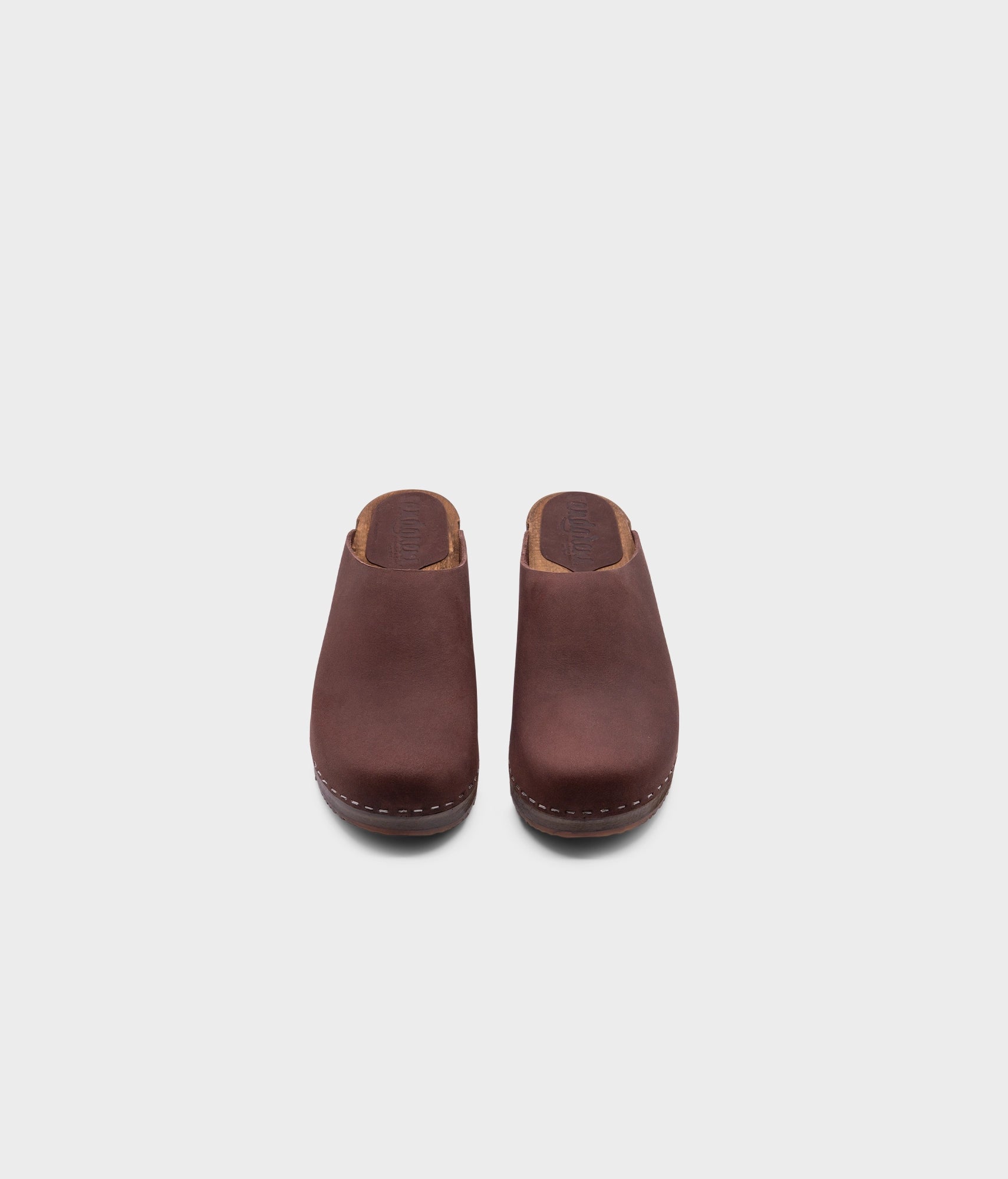 low heeled minimalistic clog mules in fudge nubuck leather stapled on a dark wooden base