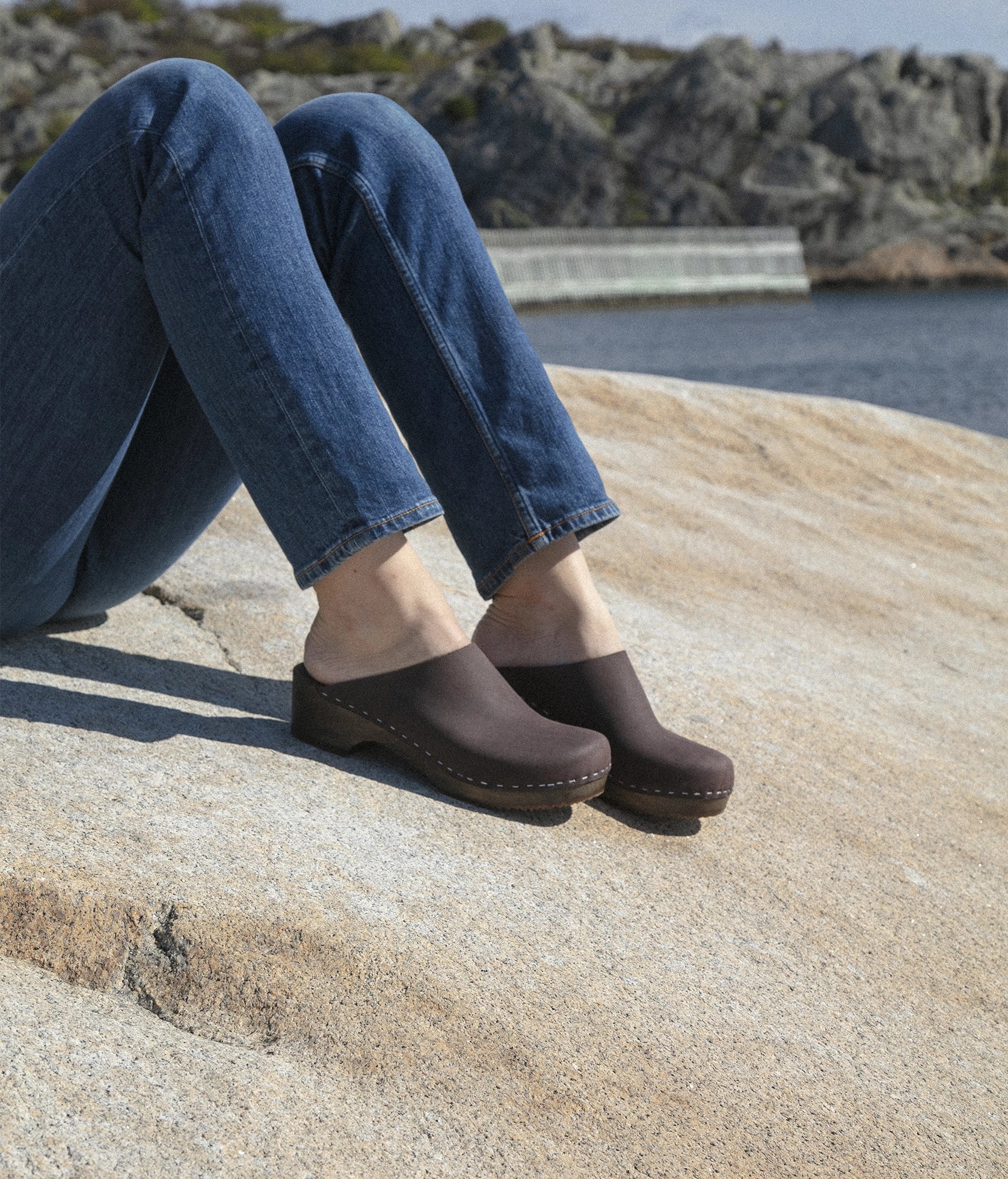 low heeled minimalistic clog mules in fudge nubuck leather stapled on a dark wooden base