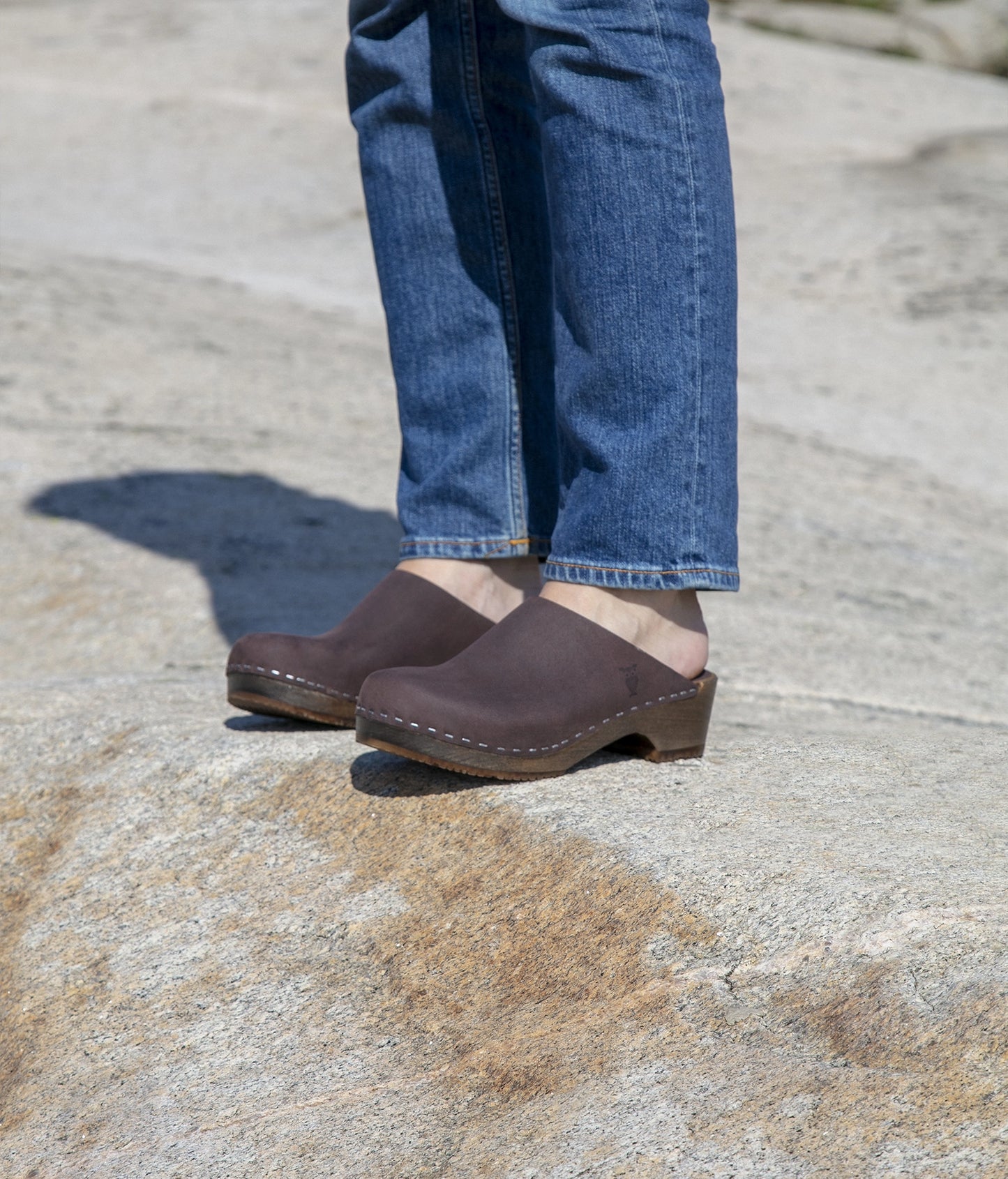 low heeled minimalistic clog mules in fudge nubuck leather stapled on a dark wooden base