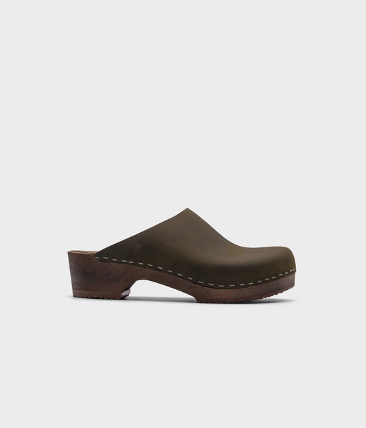 low heeled minimalistic clog mules in olive nubuck leather stapled on a dark wooden base