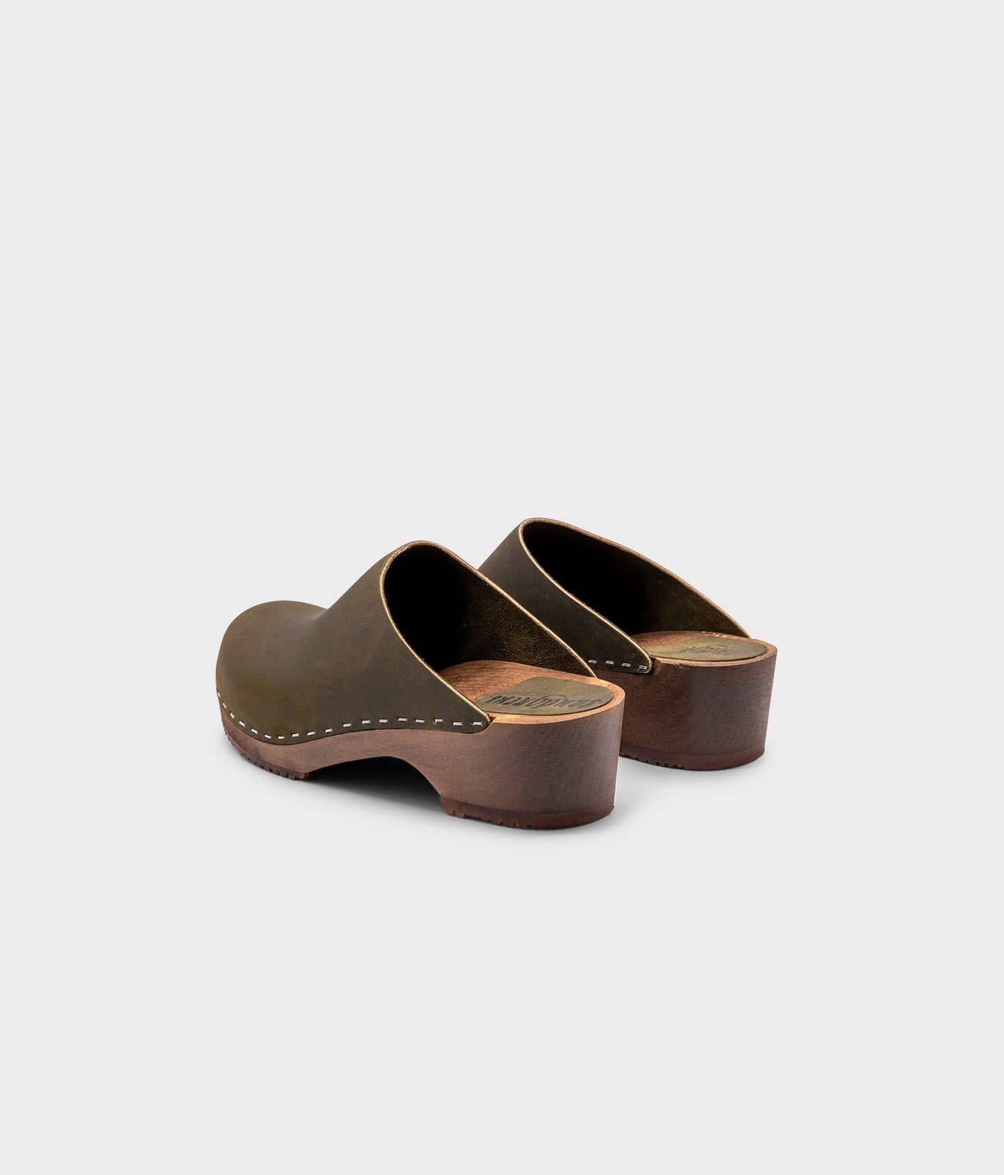 low heeled minimalistic clog mules in olive nubuck leather stapled on a dark wooden base
