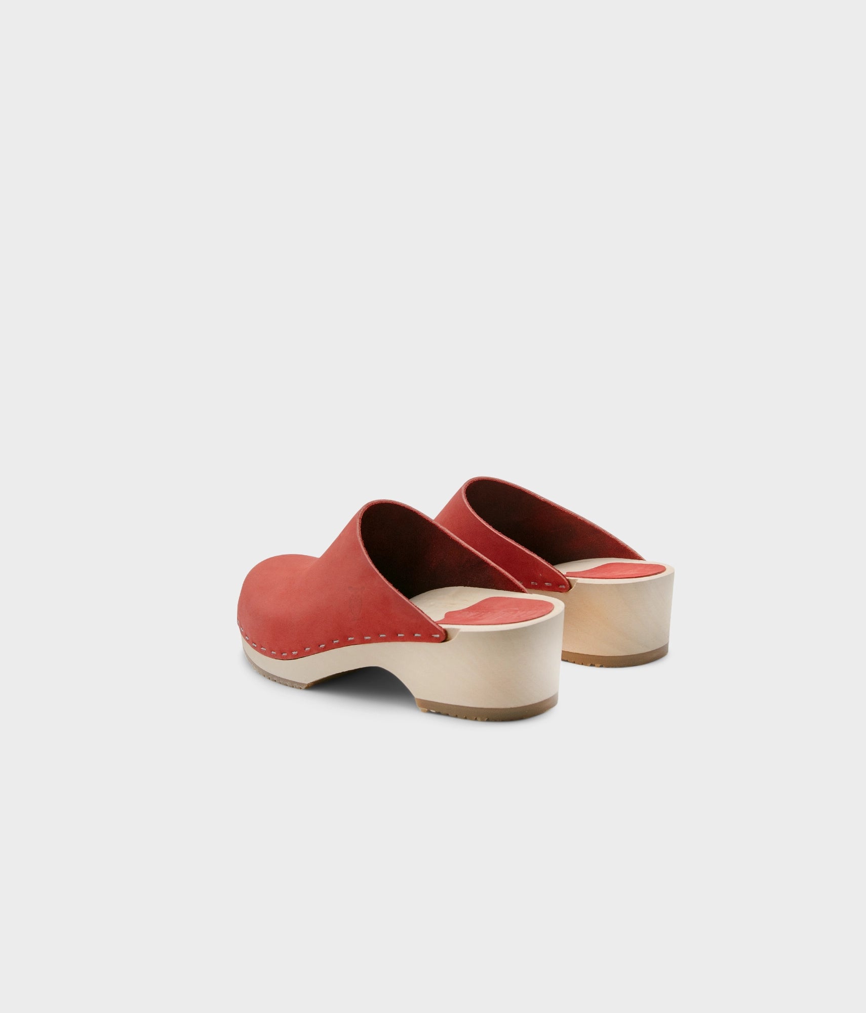 low heeled minimalistic clog mules in red nubuck leather stapled on a light wooden base