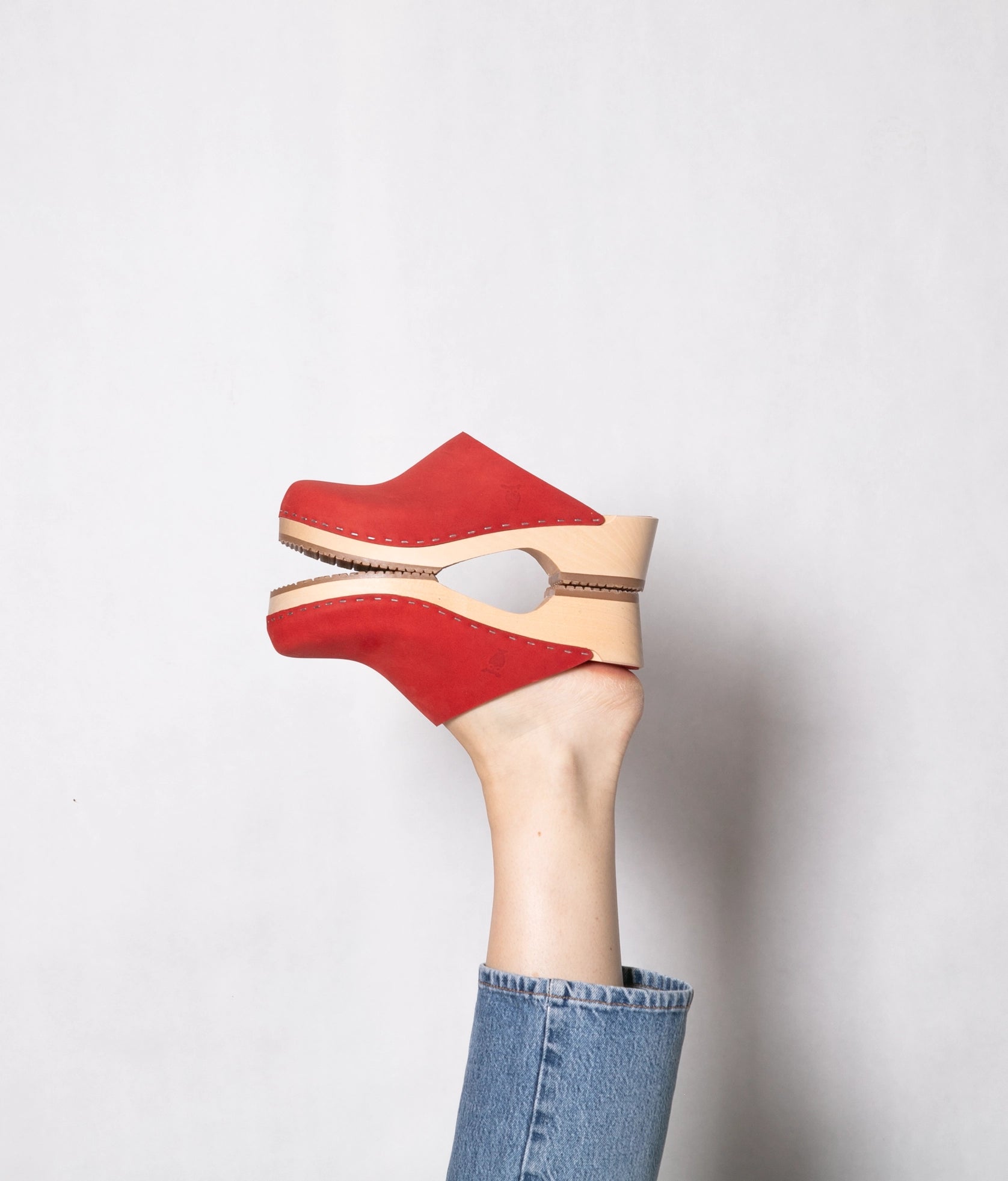 low heeled minimalistic clog mules in red nubuck leather stapled on a light wooden base