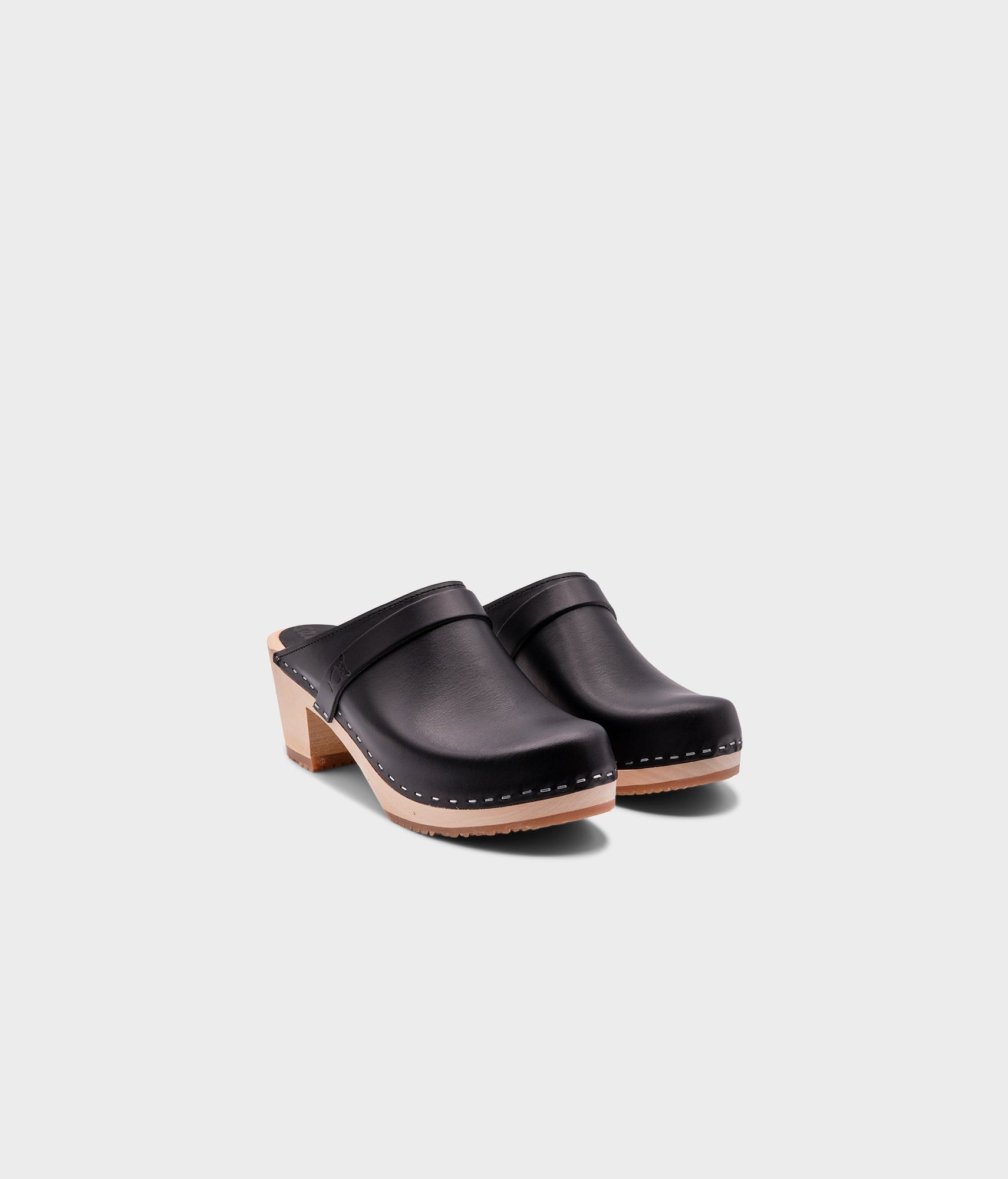 classic high heeled clog mule in black vegetable tanned leather stapled on a light wooden base with a leather strap