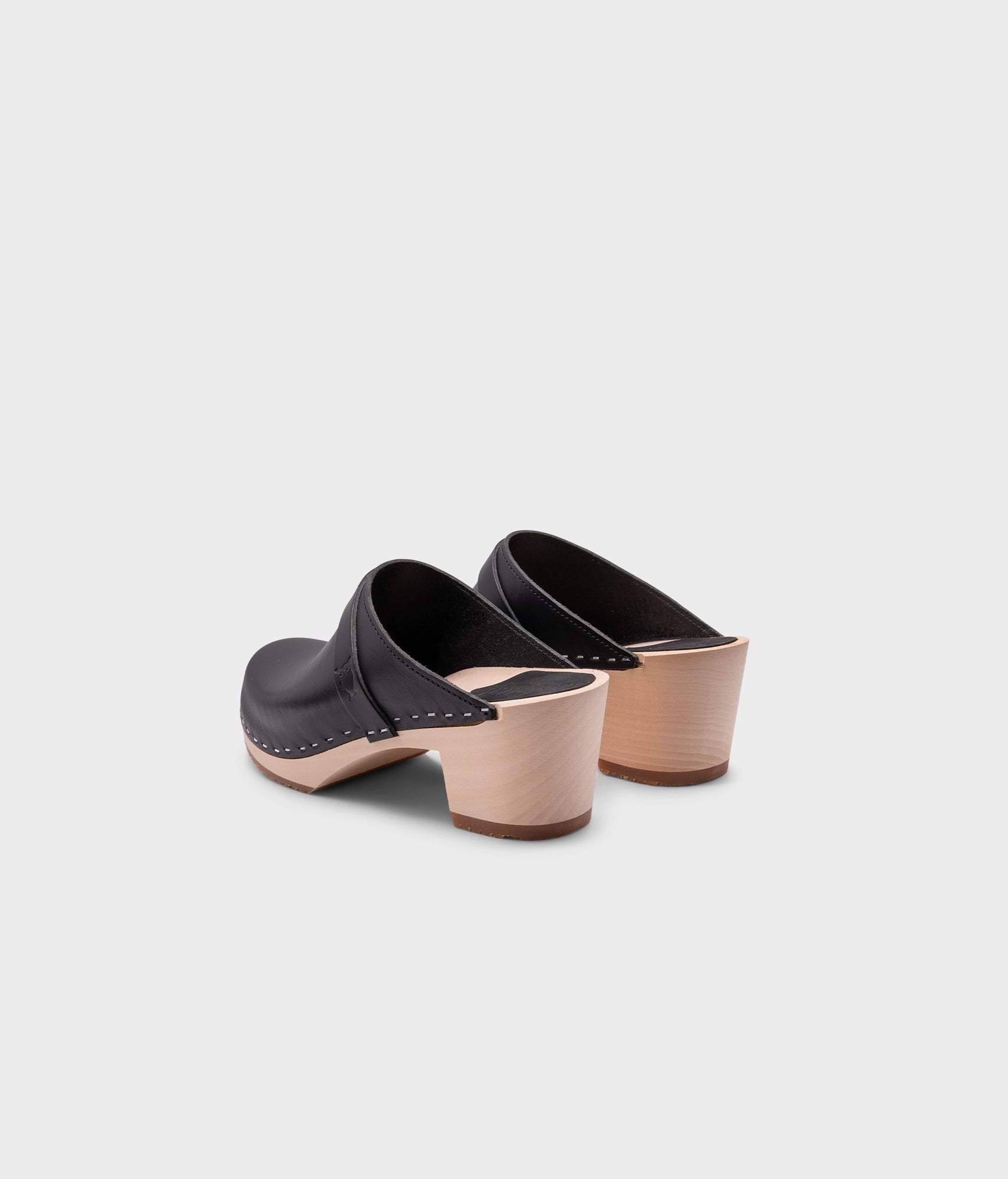 classic high heeled clog mule in black vegetable tanned leather stapled on a light wooden base with a leather strap
