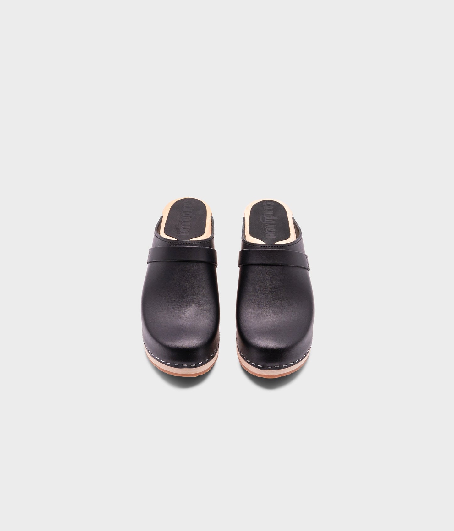 classic high heeled clog mule in black vegetable tanned leather stapled on a light wooden base with a leather strap