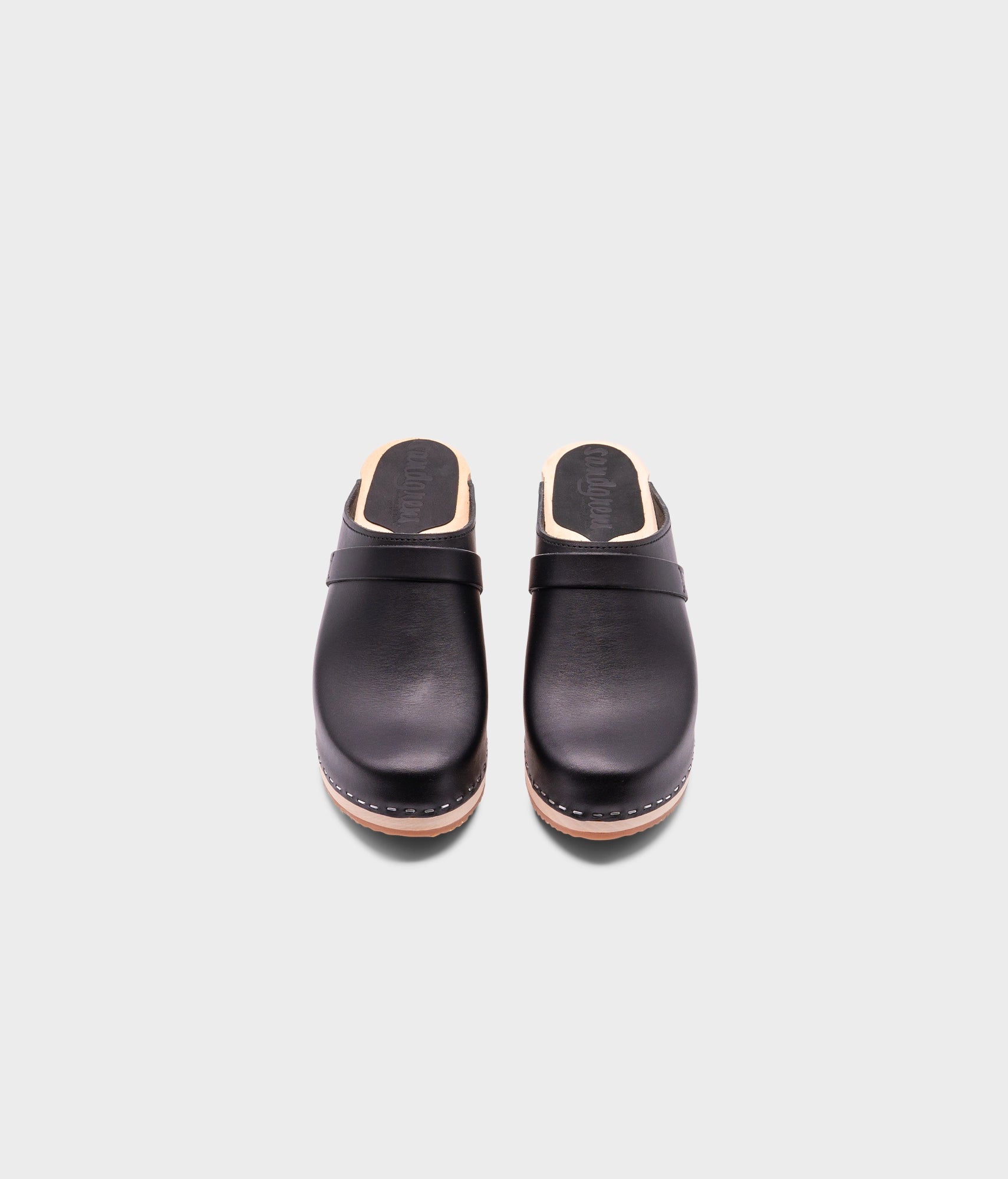 classic high heeled clog mule in black vegetable tanned leather stapled on a light wooden base with a leather strap
